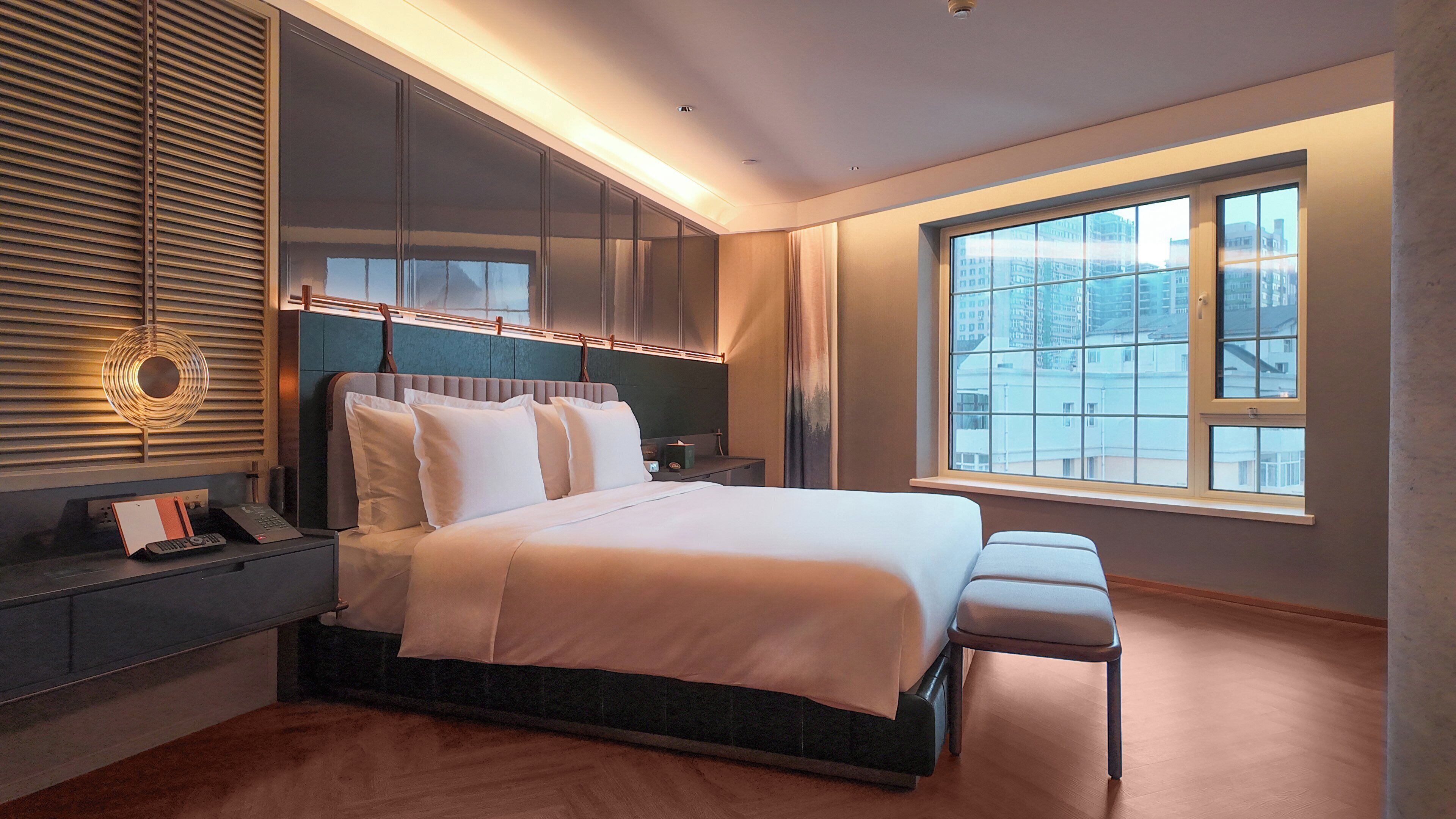 Un dormitorio moderno con una cama grande, armario empotrado, mesitas de noche y un amplio ventanal con vistas a la ciudad.