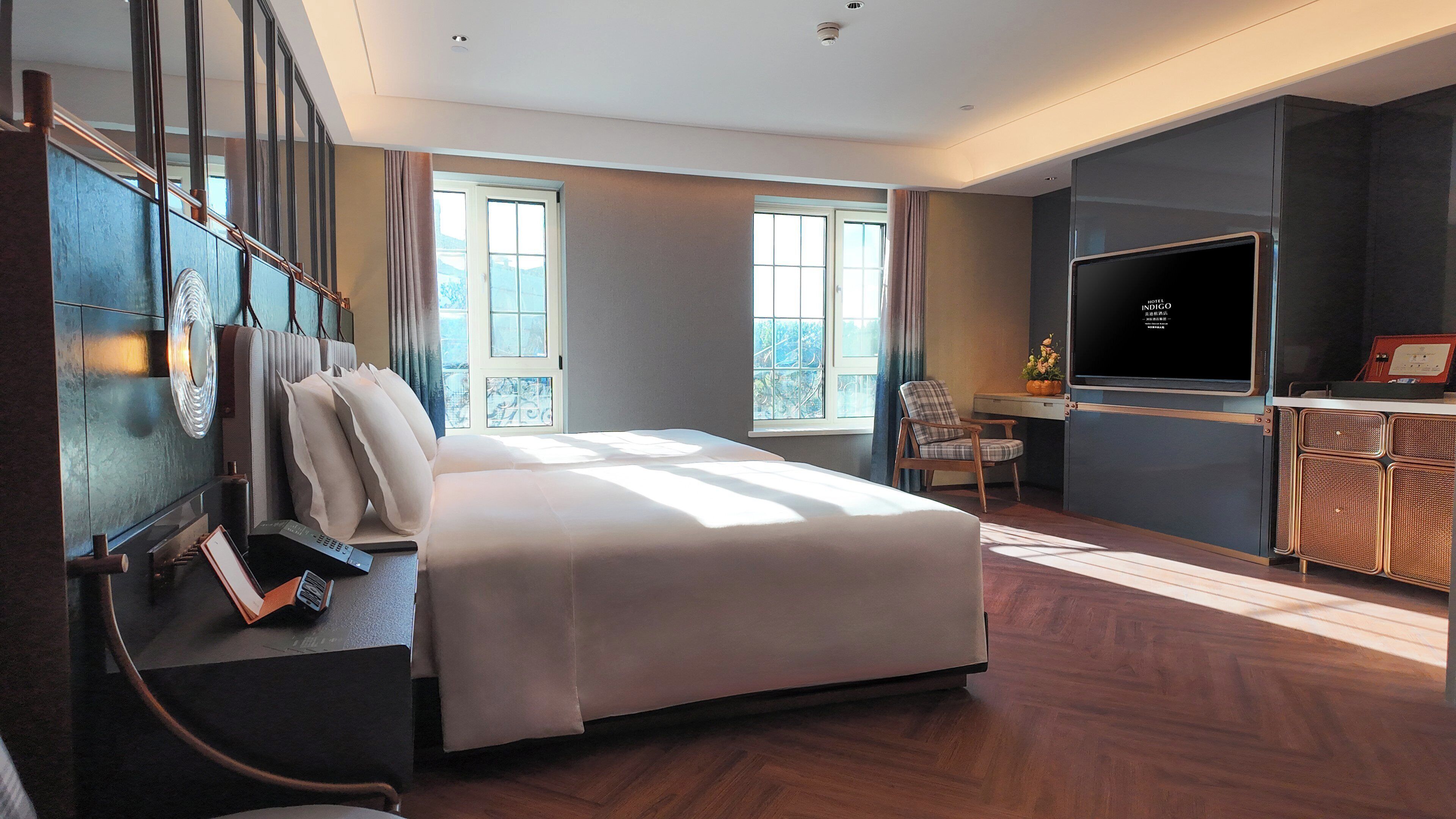 A modern hotel room with a large bed, a desk with a chair, a television, and a view of the outdoors.