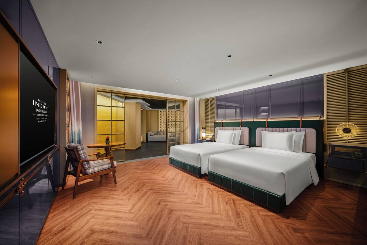 Une chambre d’hôtel avec deux lits, une télévision, un plancher en bois et une vue sur le couloir.