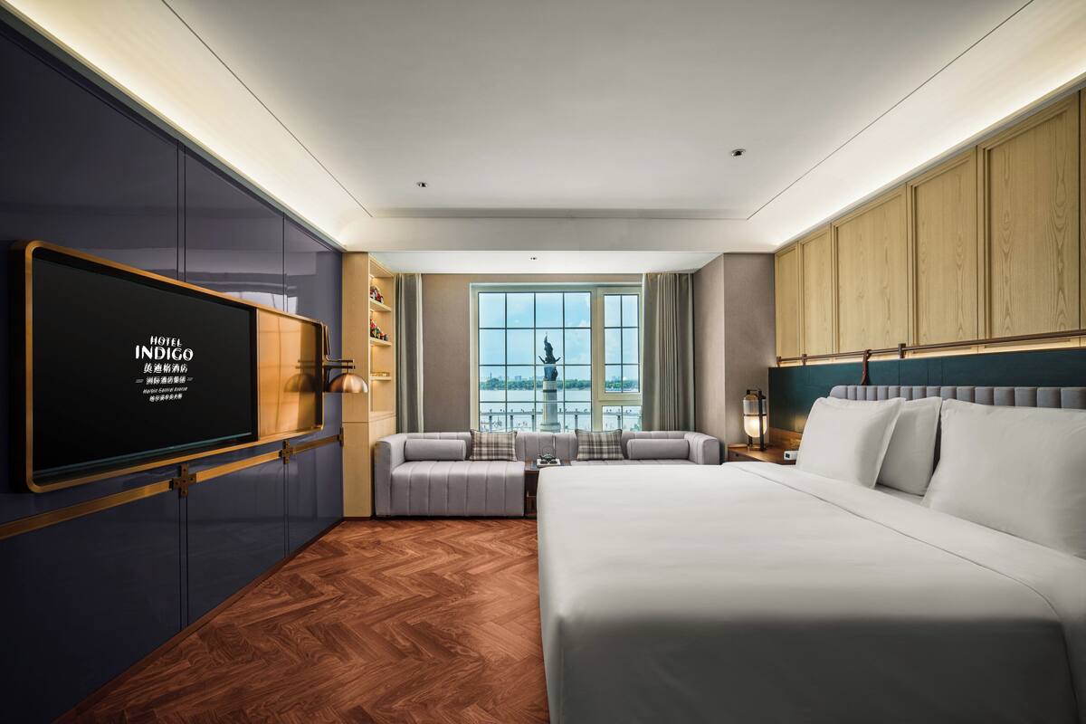 A hotel room with a bed, a sofa, a TV, and a window with a view.