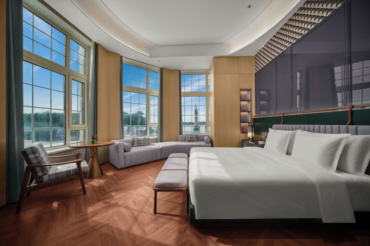 Un dormitorio amplio con una cama grande, un área de descanso y vistas a la silueta urbana.