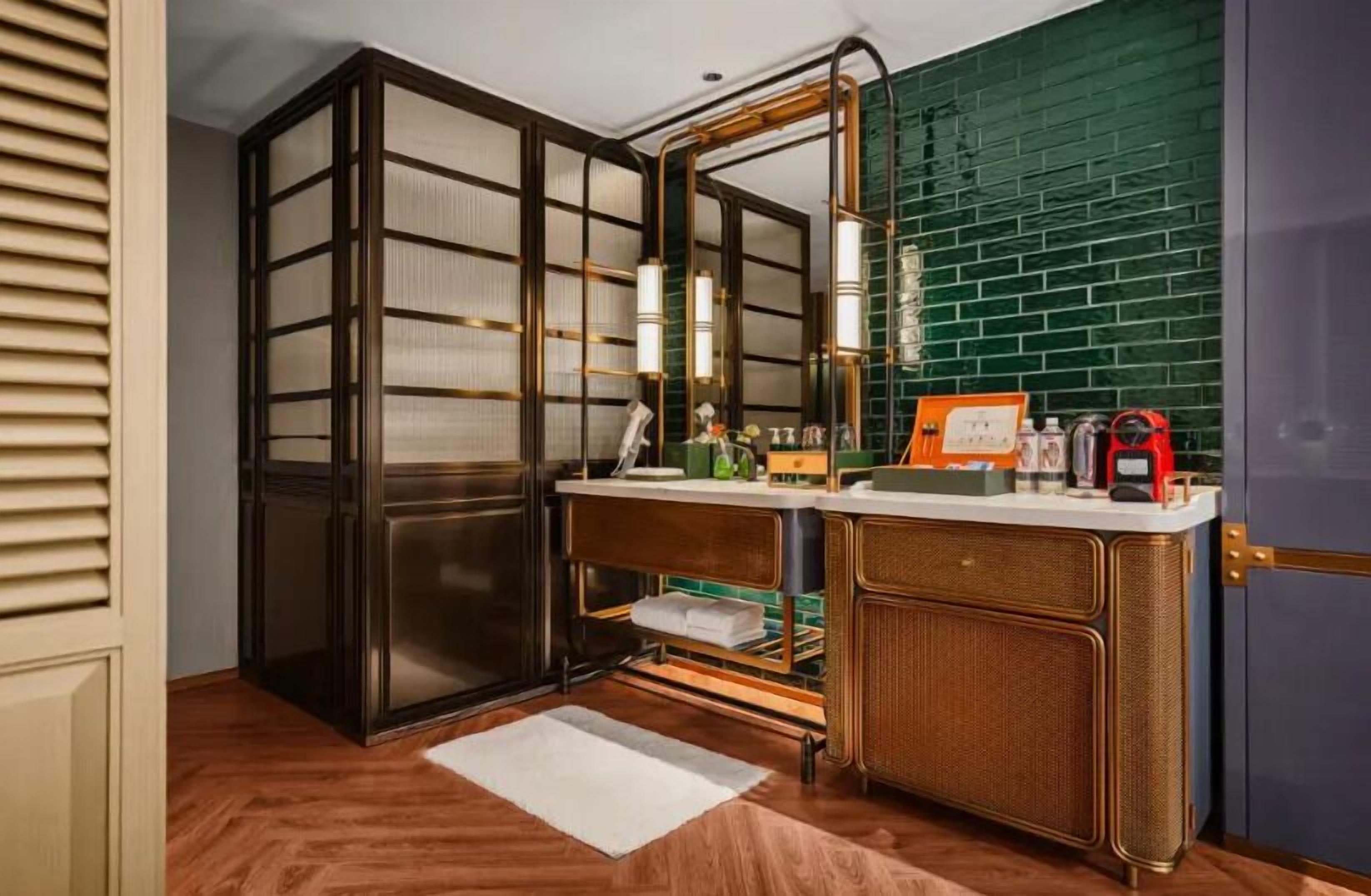 A bathroom with a wooden vanity, a mirror, and a green tiled wall.