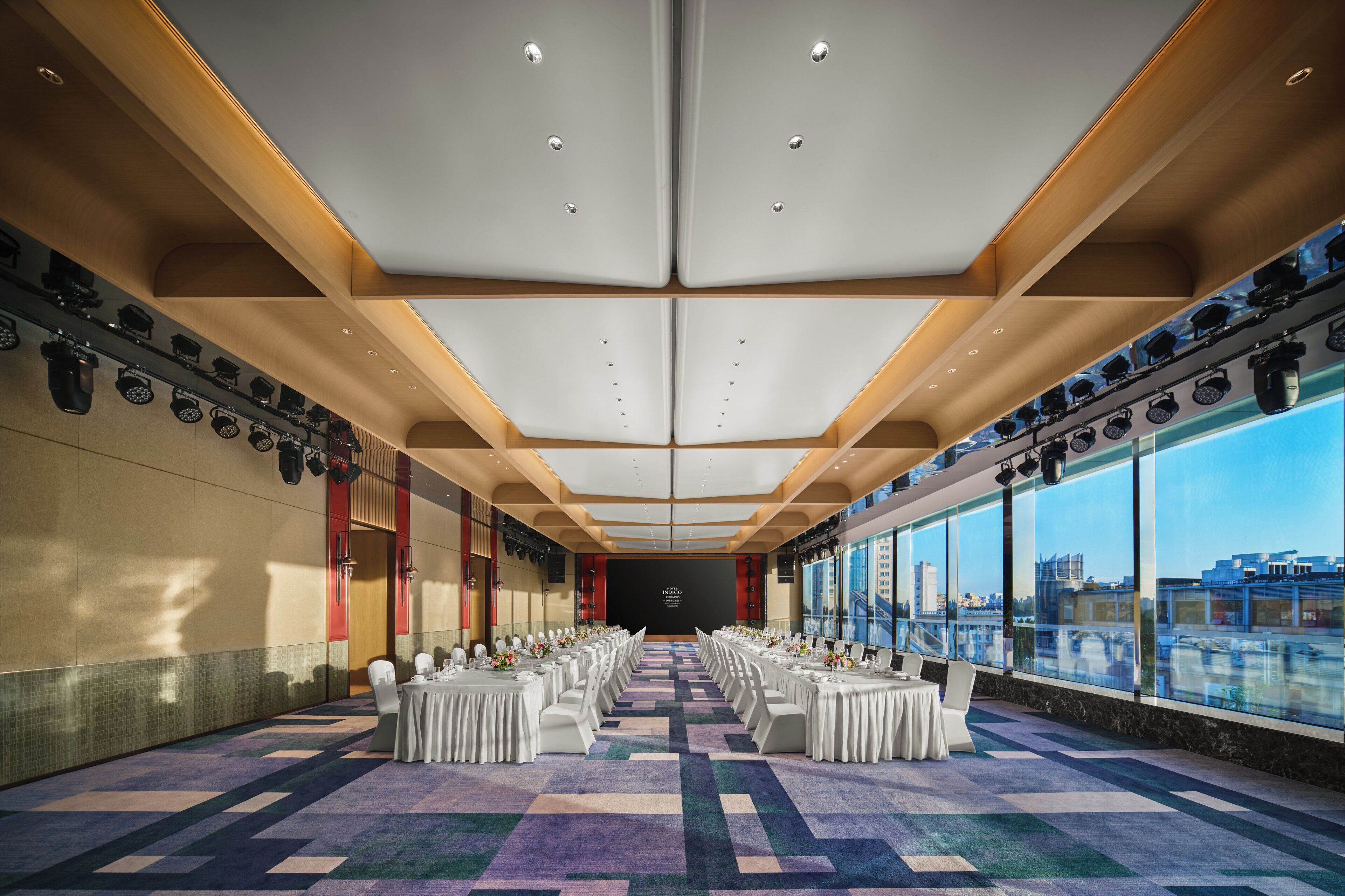 A large, well-lit conference room with a long table set for a meeting, large windows offering a city view, and a modern ceiling design.