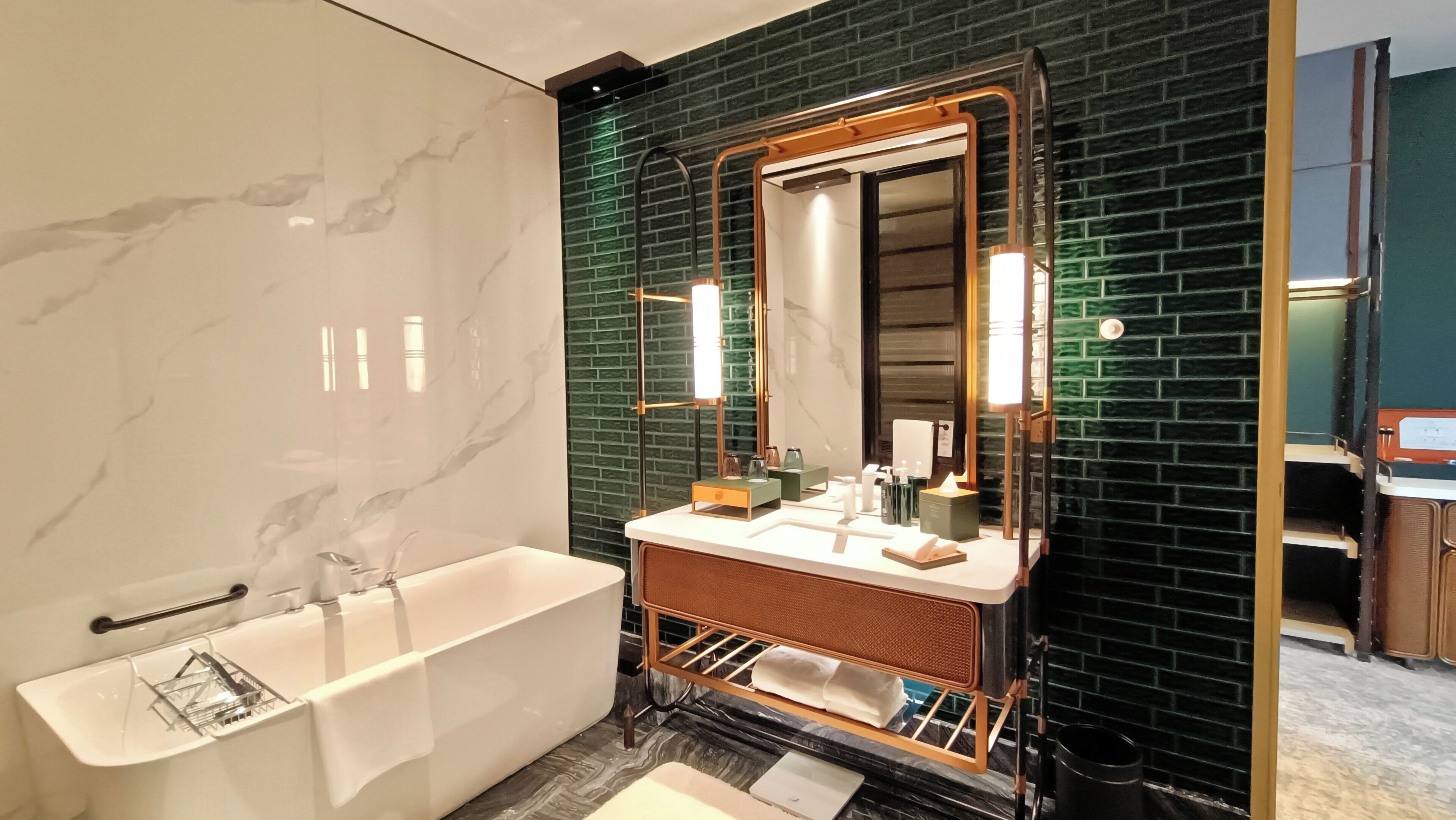Un baño moderno con una bañera independiente, un lavabo con espejo y una pared de ladrillo verde.