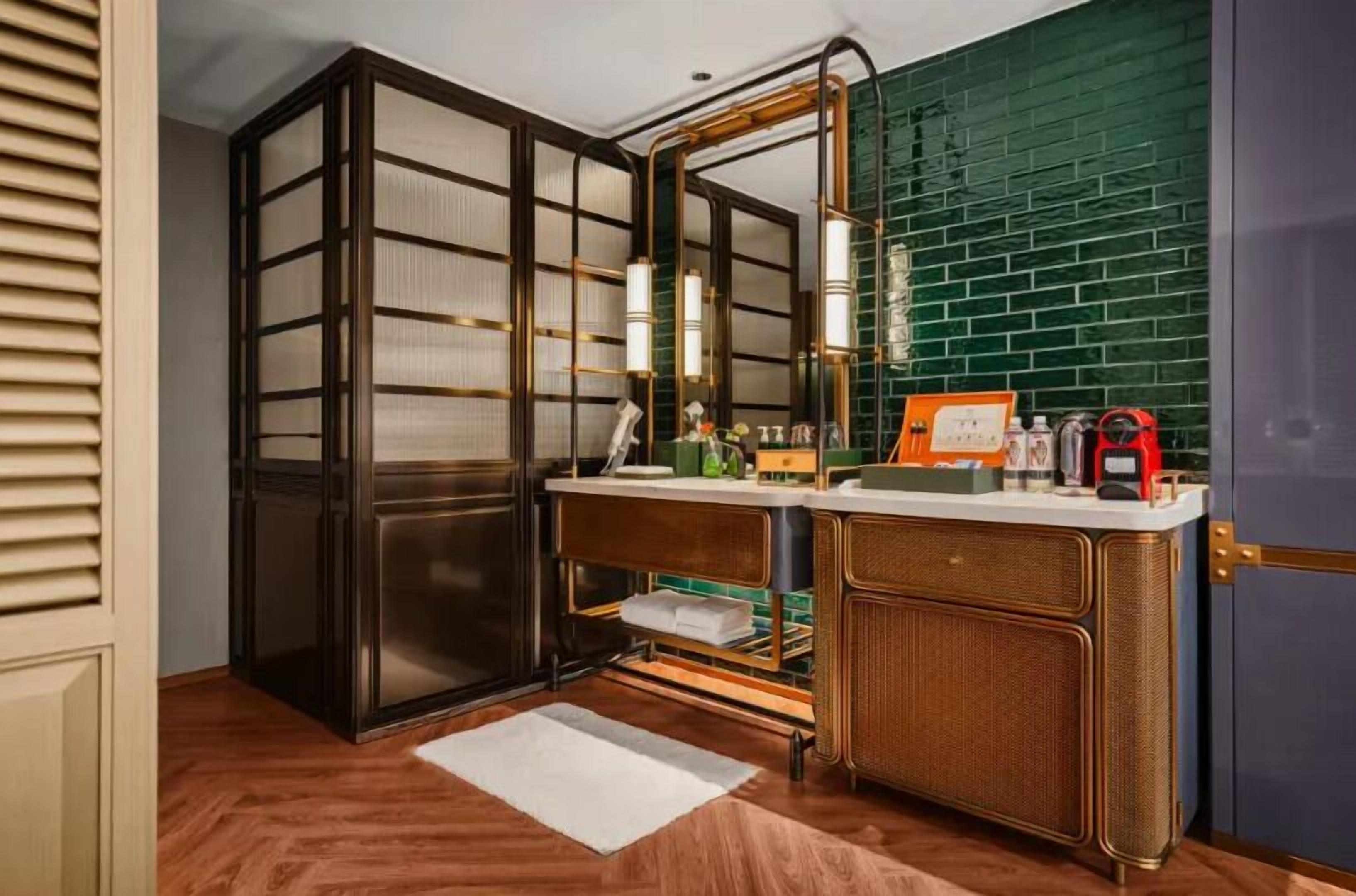 Une salle de bain moderne avec un grand miroir, des meubles en bois et un mur recouvert de carreaux verts.