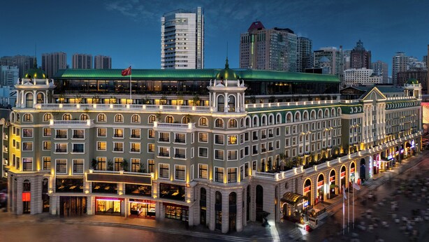 Un hotel histórico con varios pisos, amplias ventanas y un techo verde destacado.
