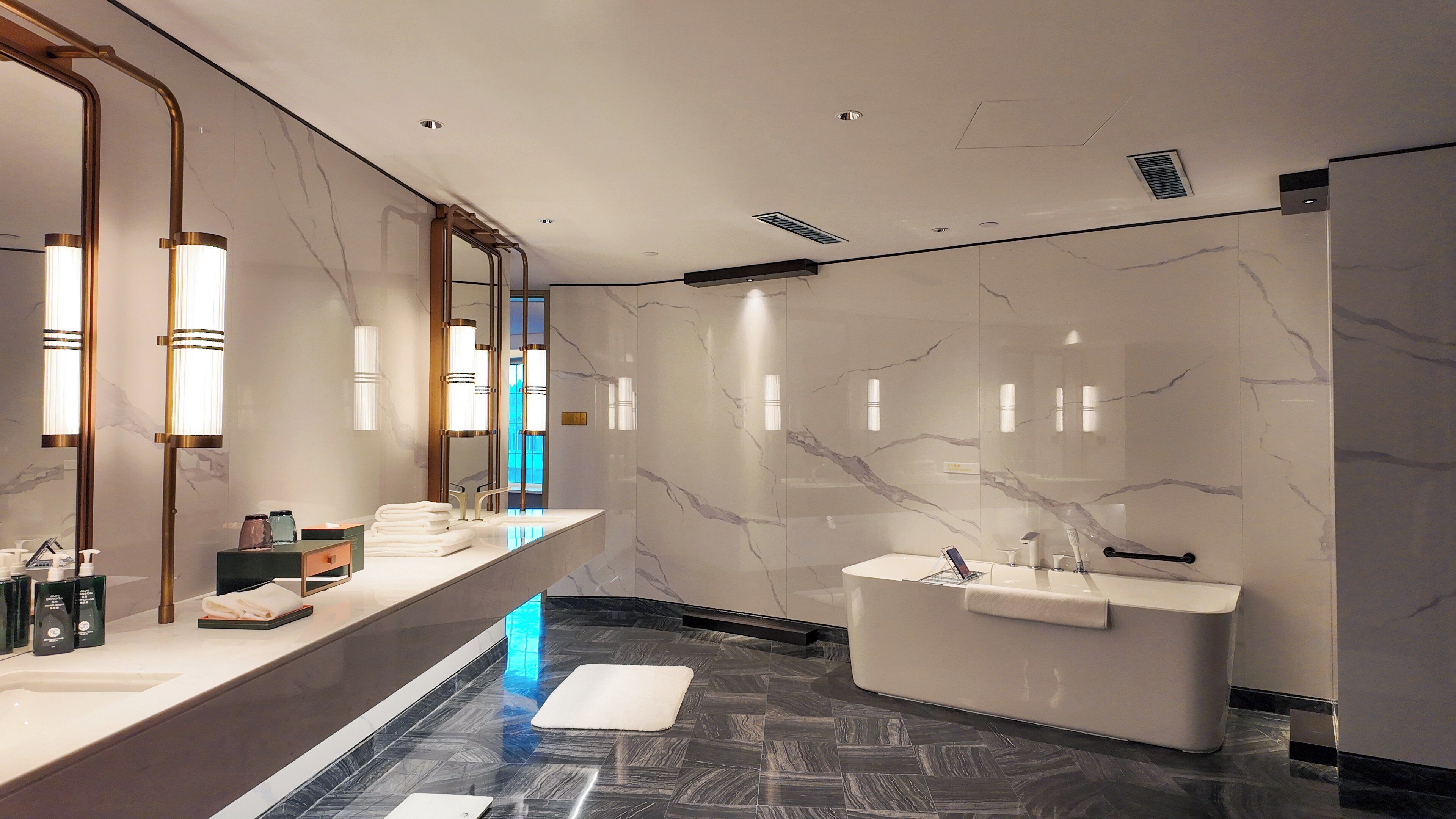 Un baño moderno con tocador de mármol, una bañera independiente y un espejo grande.