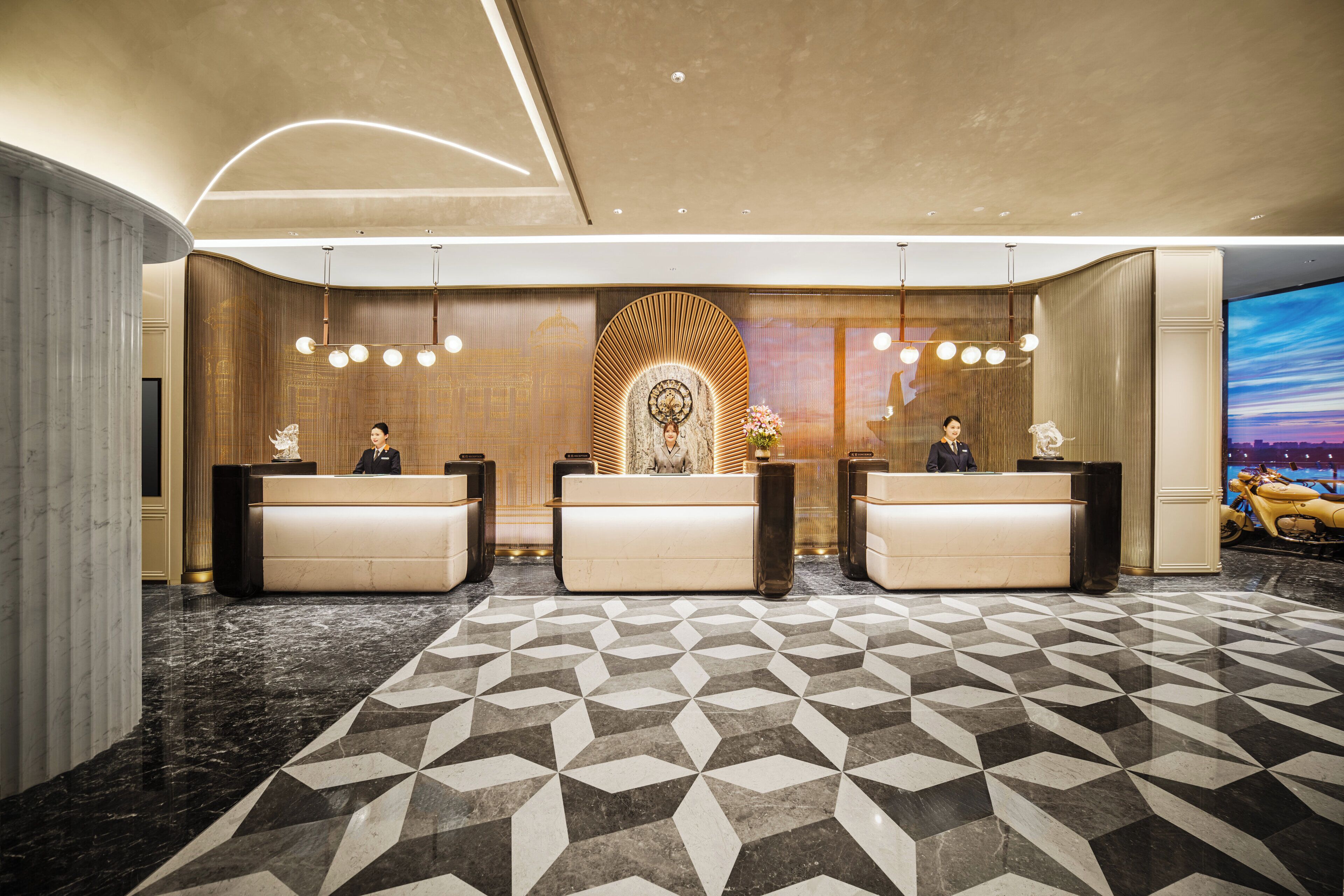 Een hotel receptie met drie balies, een vloer met patroon en een groot scherm waarop een stadsgezicht te zien is.