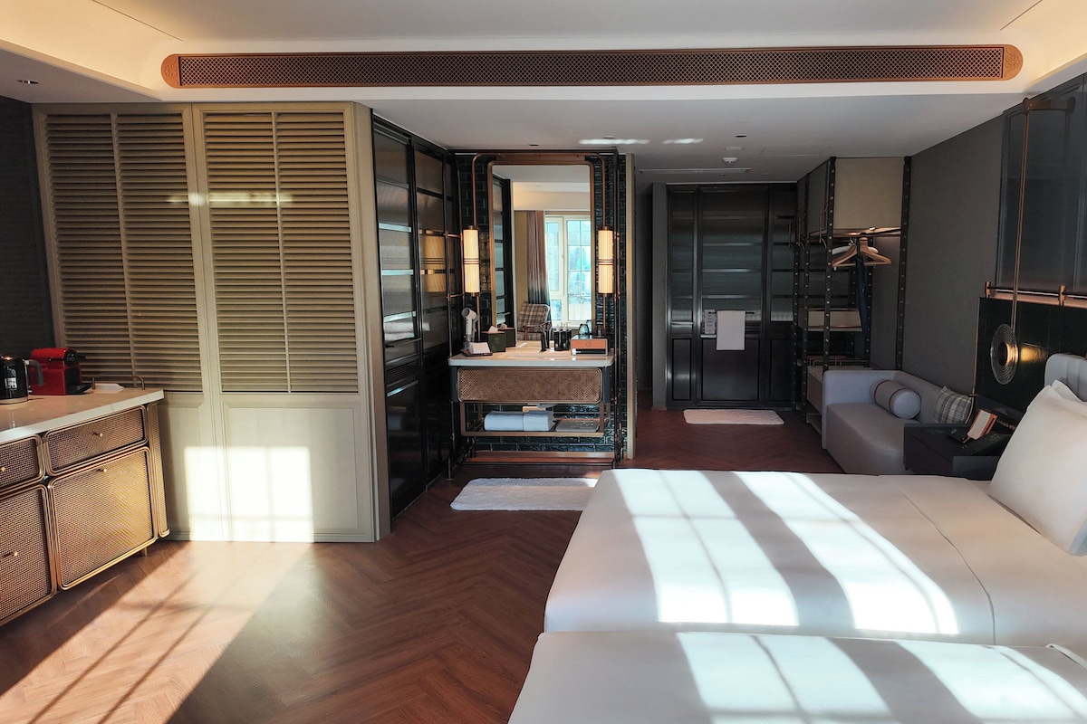 Una habitación de hotel moderna con una cama grande, un rincón de descanso, una kitchenette y un vestidor.