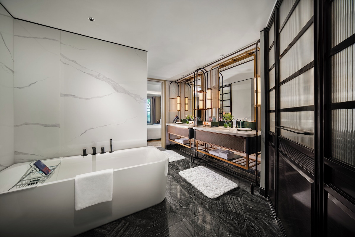 Un baño moderno con una bañera grande, un tocador con espejo y una pared de mármol.