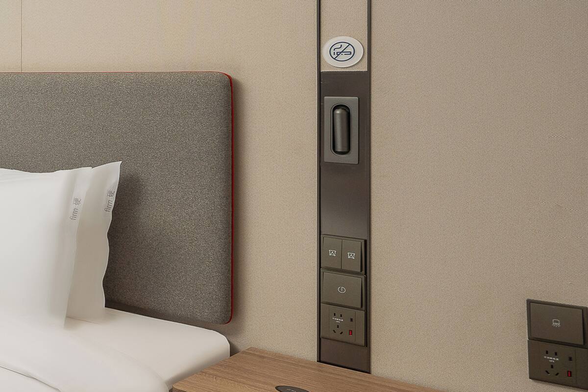 Una camera d'albergo con un letto, una testiera, un pannello di controllo a parete con pulsanti e una presa di corrente.