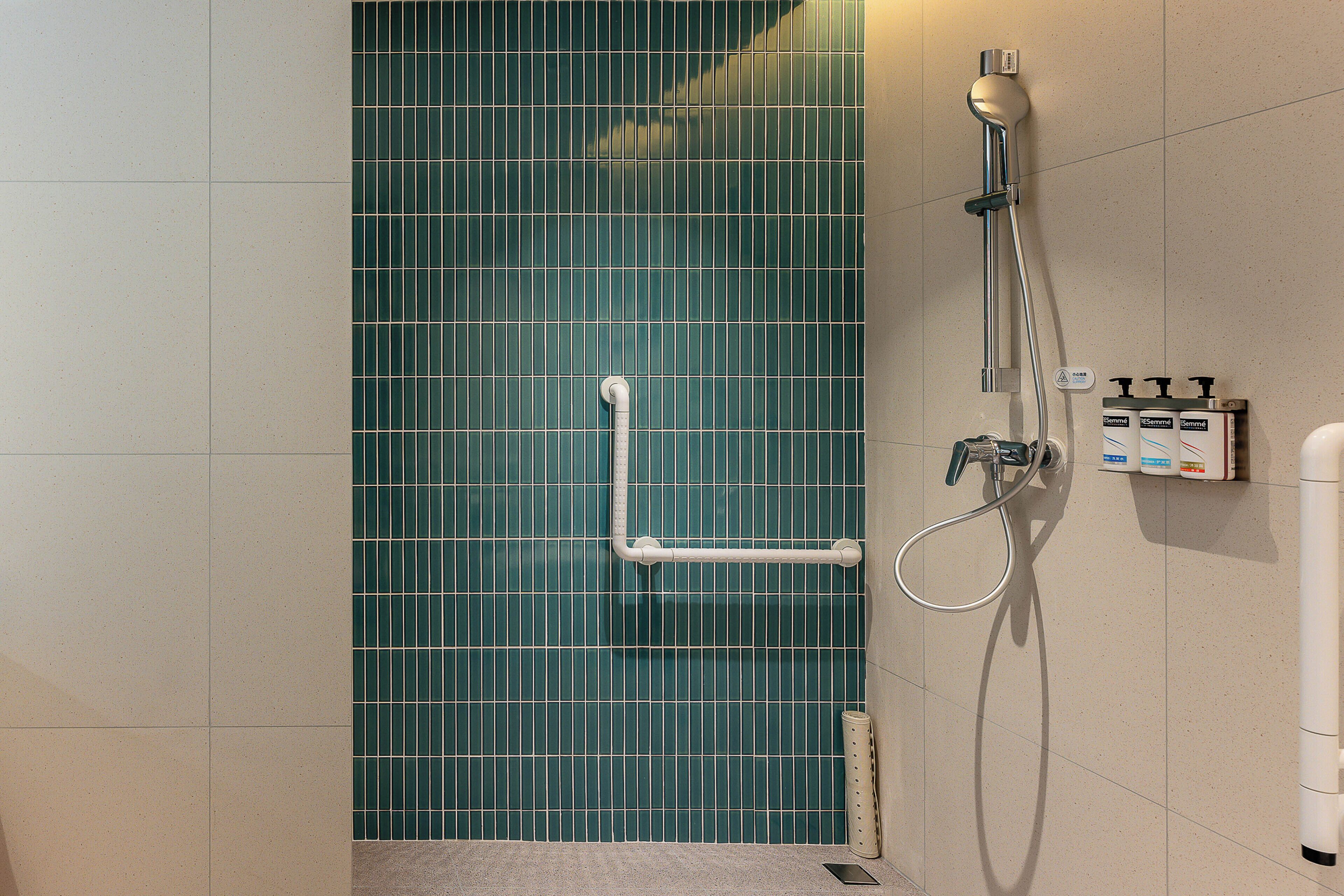 A shower area with a green tiled wall, a handheld showerhead, a wall-mounted faucet, and a handheld shower hose.