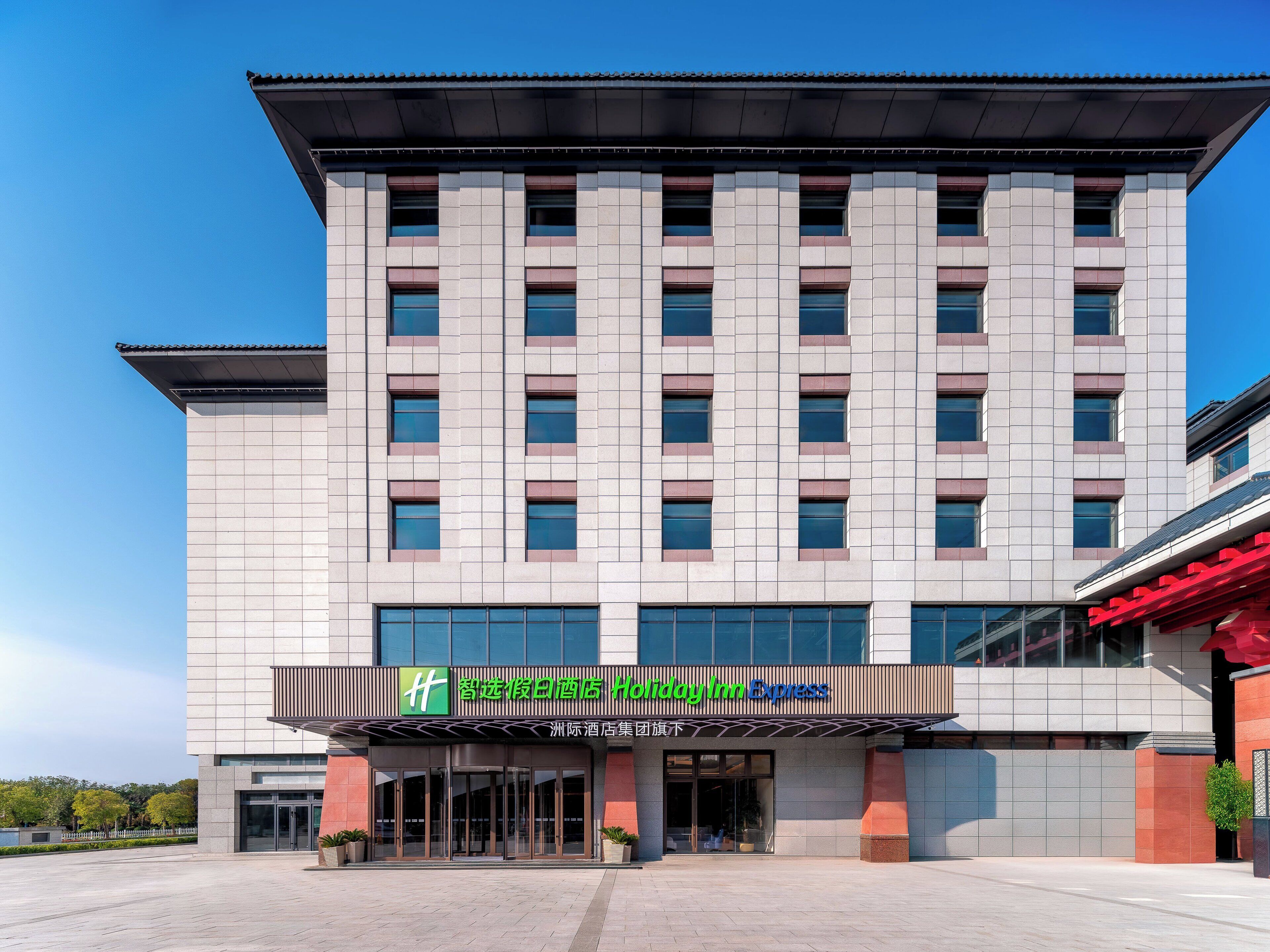 Un moderno edificio de hotel con fachada plana, grandes ventanales y una entrada destacada con un letrero verde.