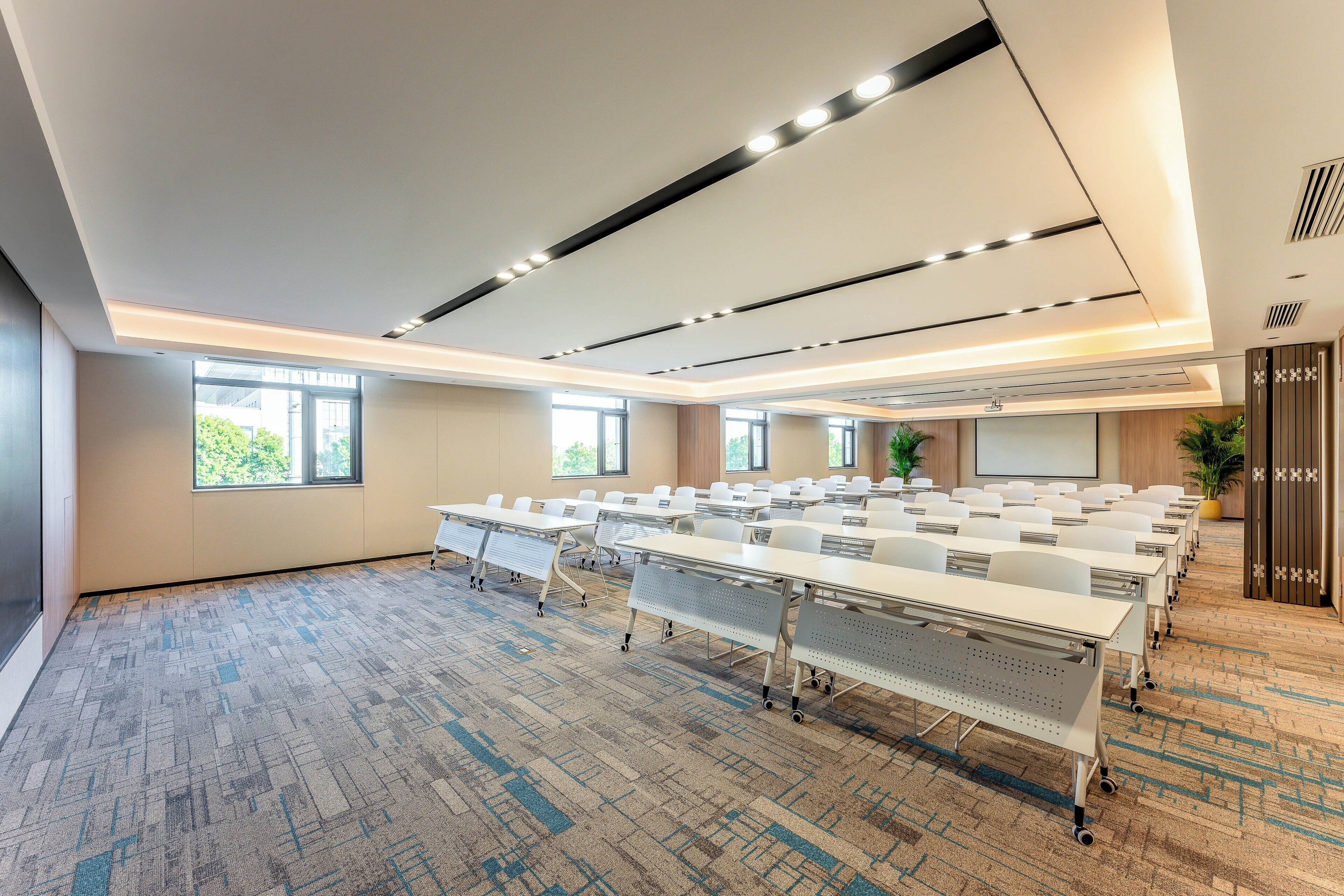 A conference room with multiple tables and chairs, large windows, and a carpeted floor.