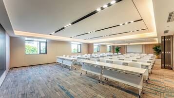 A conference room with multiple tables and chairs, large windows, and a carpeted floor.