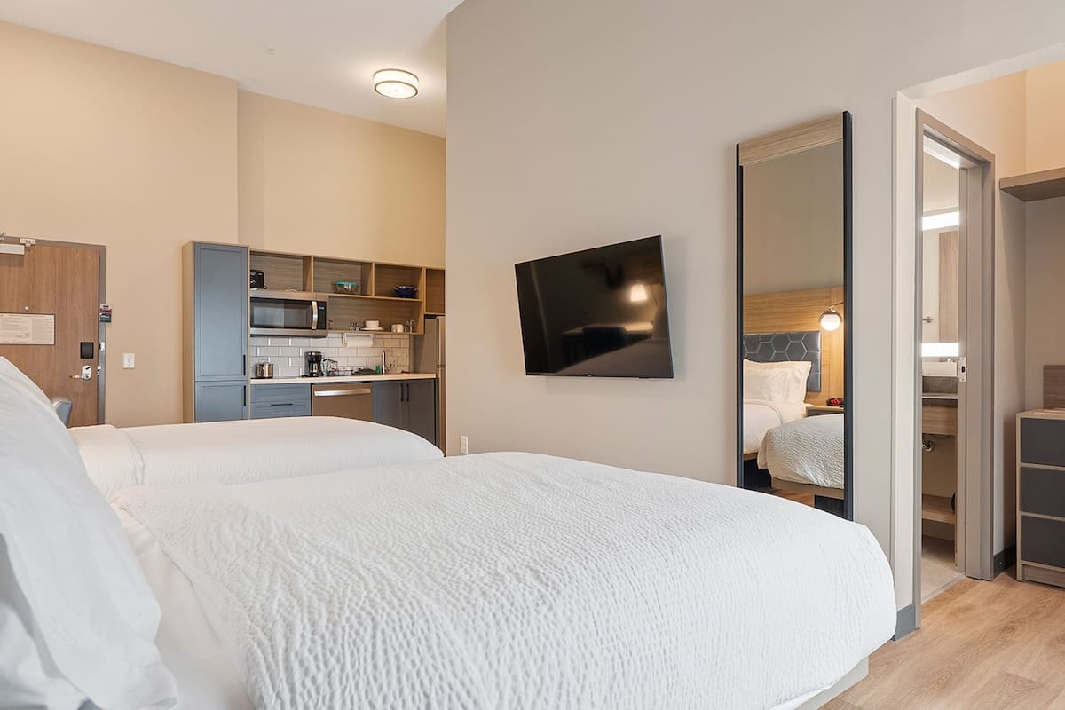 A hotel room with a large bed, a TV mounted on the wall, a separate bathroom, and a kitchenette.