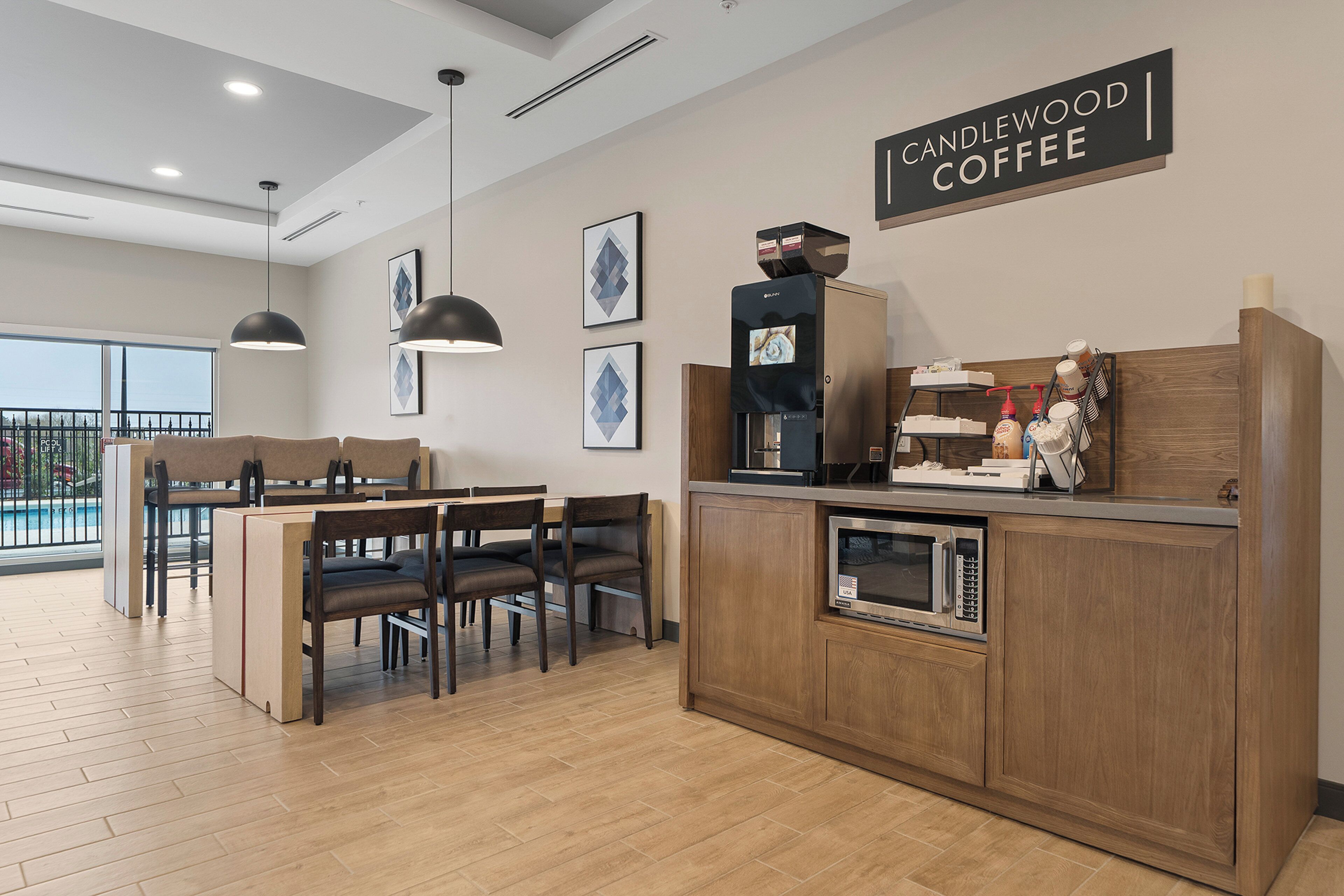 A modern kitchen with a coffee station, wooden cabinets, and a dining area with a pool view.