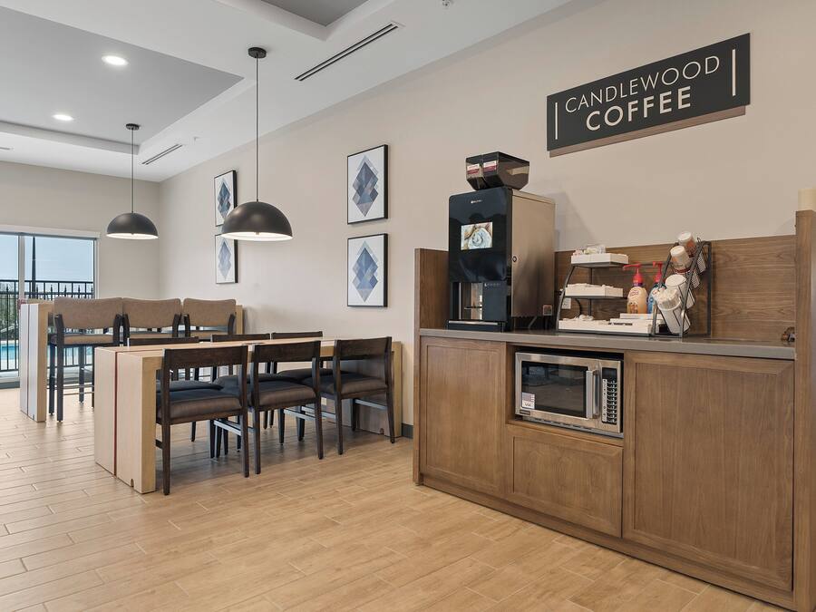 A modern kitchen with a coffee station, wooden cabinets, and a dining area with a pool view.
