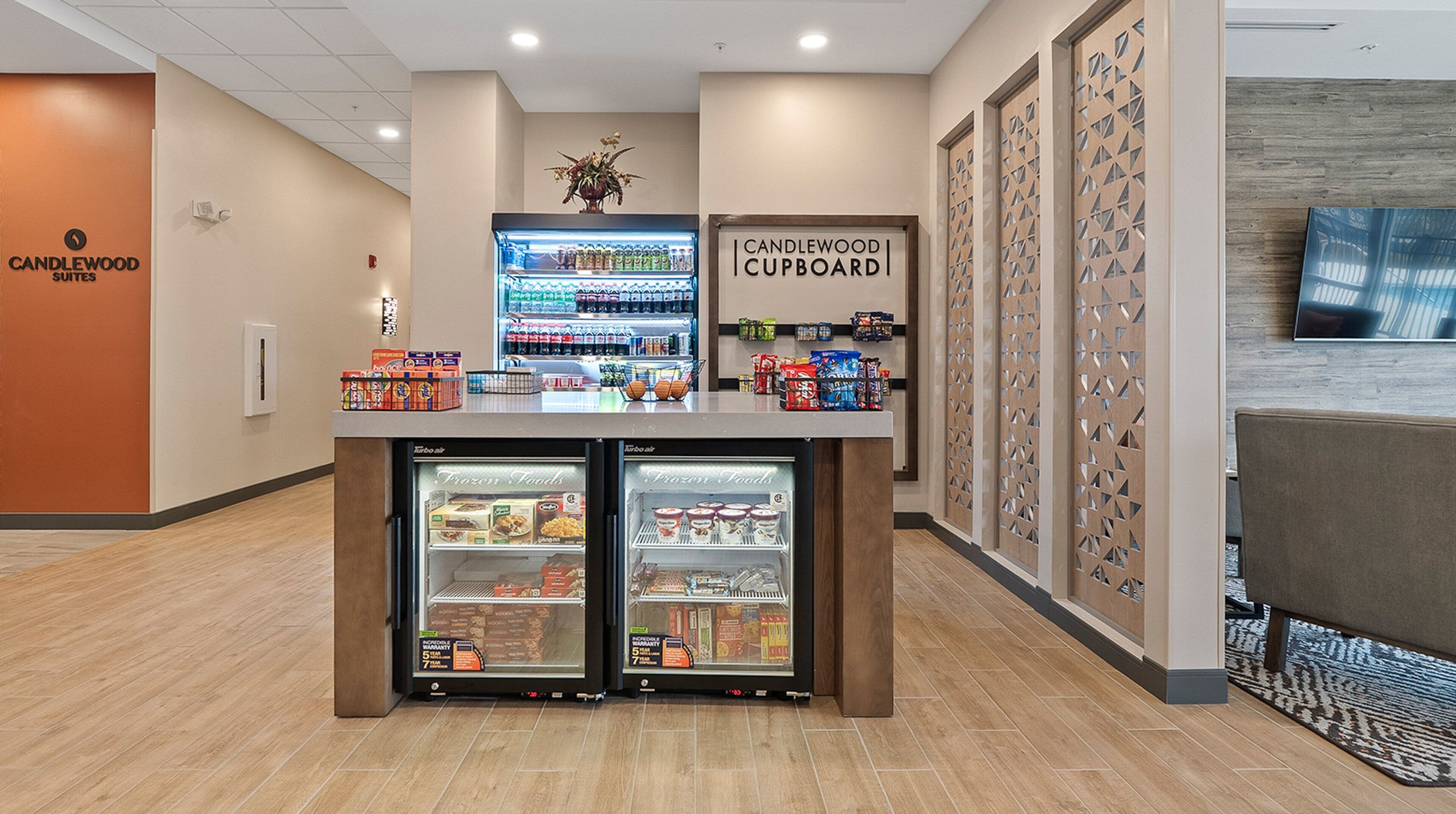 Eine Hotellobby mit einem Schild 'Candlewood Cupboard', einem Kühlvitrine mit Tiefkühlkost und einem Schild 'Candlewood Suites' an der Wand.