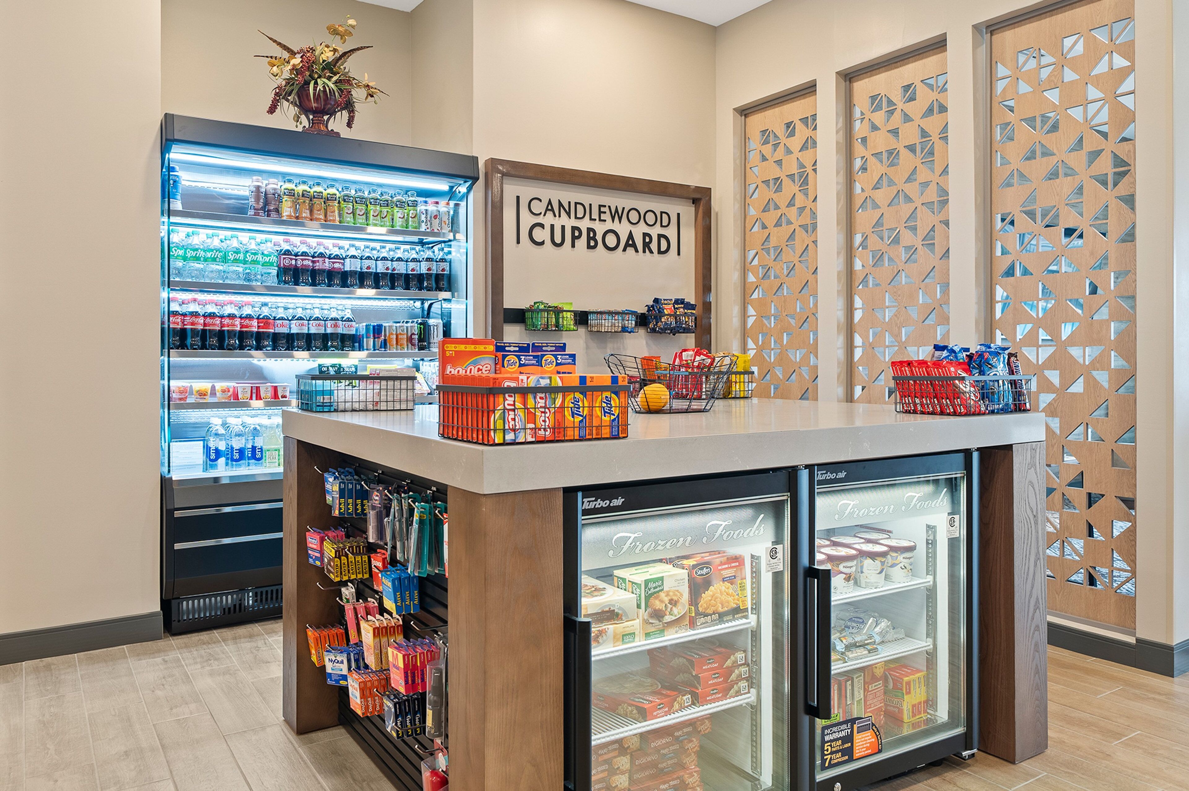 A self-service beverage station with a variety of drinks and snacks, a refrigerated section for frozen foods, and a display for candles and other items.
