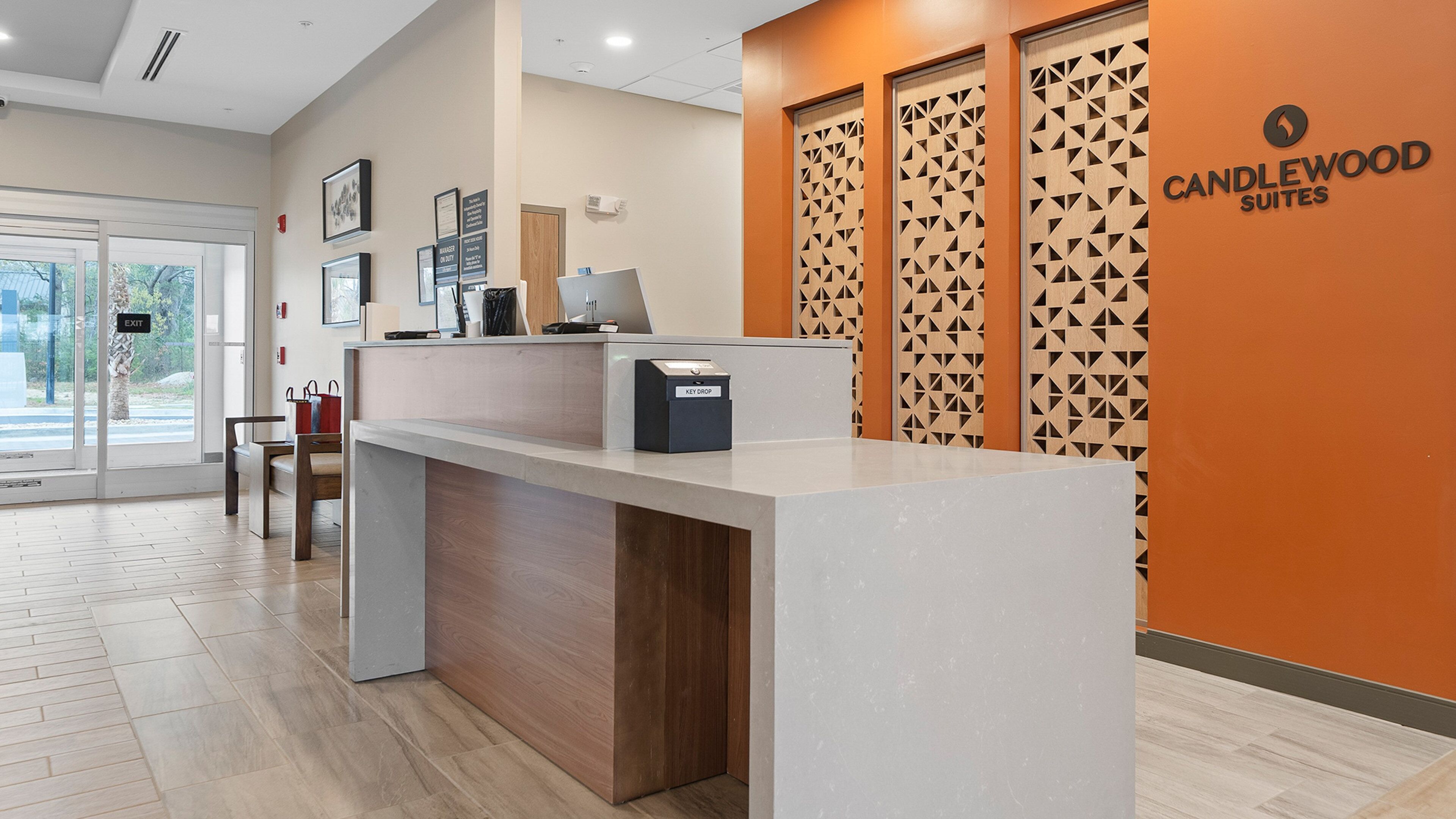 A reception desk with a modern design, a key drop box, framed certificates on the wall, and a sign for the exit.