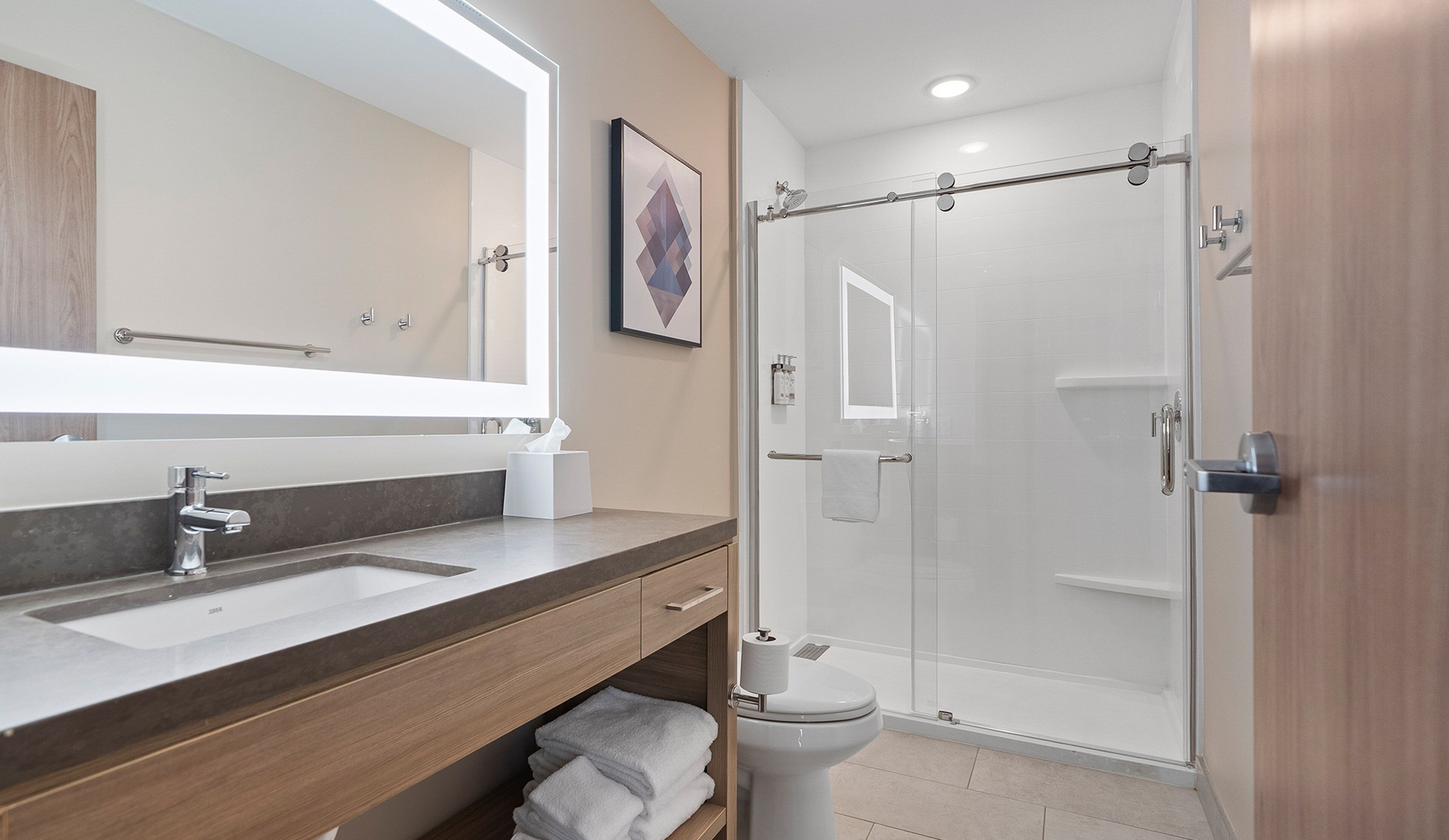 Un baño moderno con un espejo grande, un lavamanos, un inodoro y una ducha con mampara de vidrio.