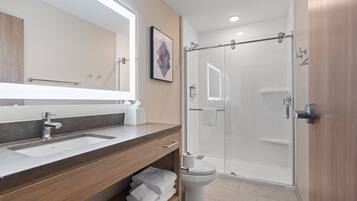 Un baño moderno con un espejo grande, un lavamanos, un inodoro y una ducha con mampara de vidrio.