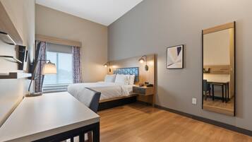 A modern hotel room with a bed, bedside table, lamp, and a large mirror.