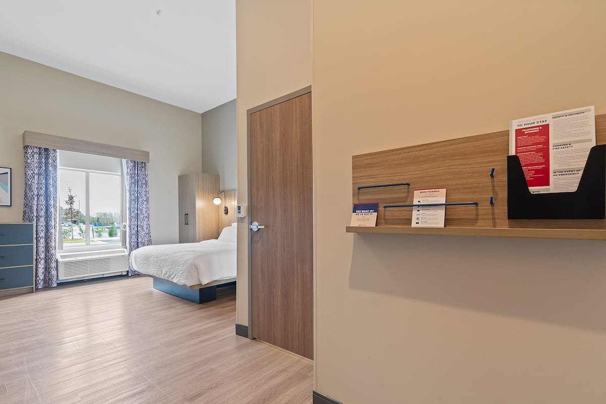 A hotel room with a bed, a desk, and a window. There is a sign on the wall with safety information.
