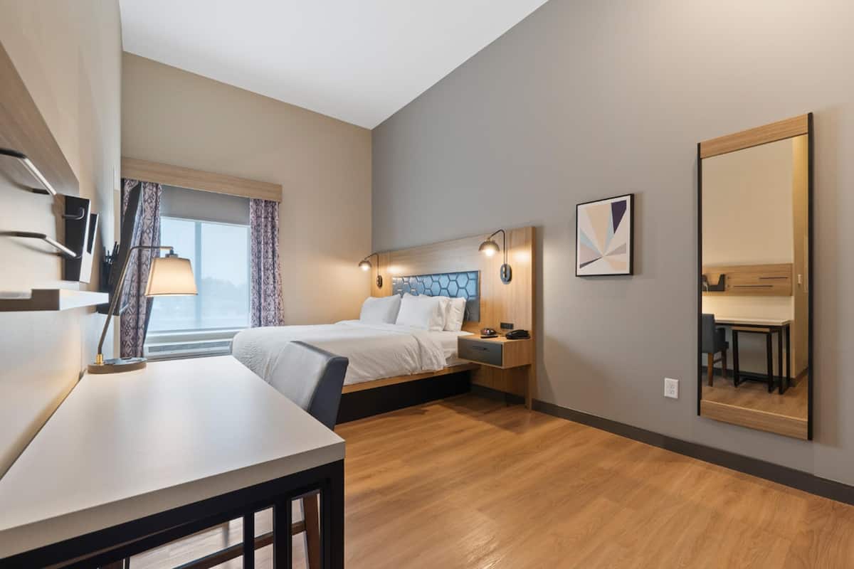 A modern hotel room with a bed, bedside table, lamp, and a large mirror.