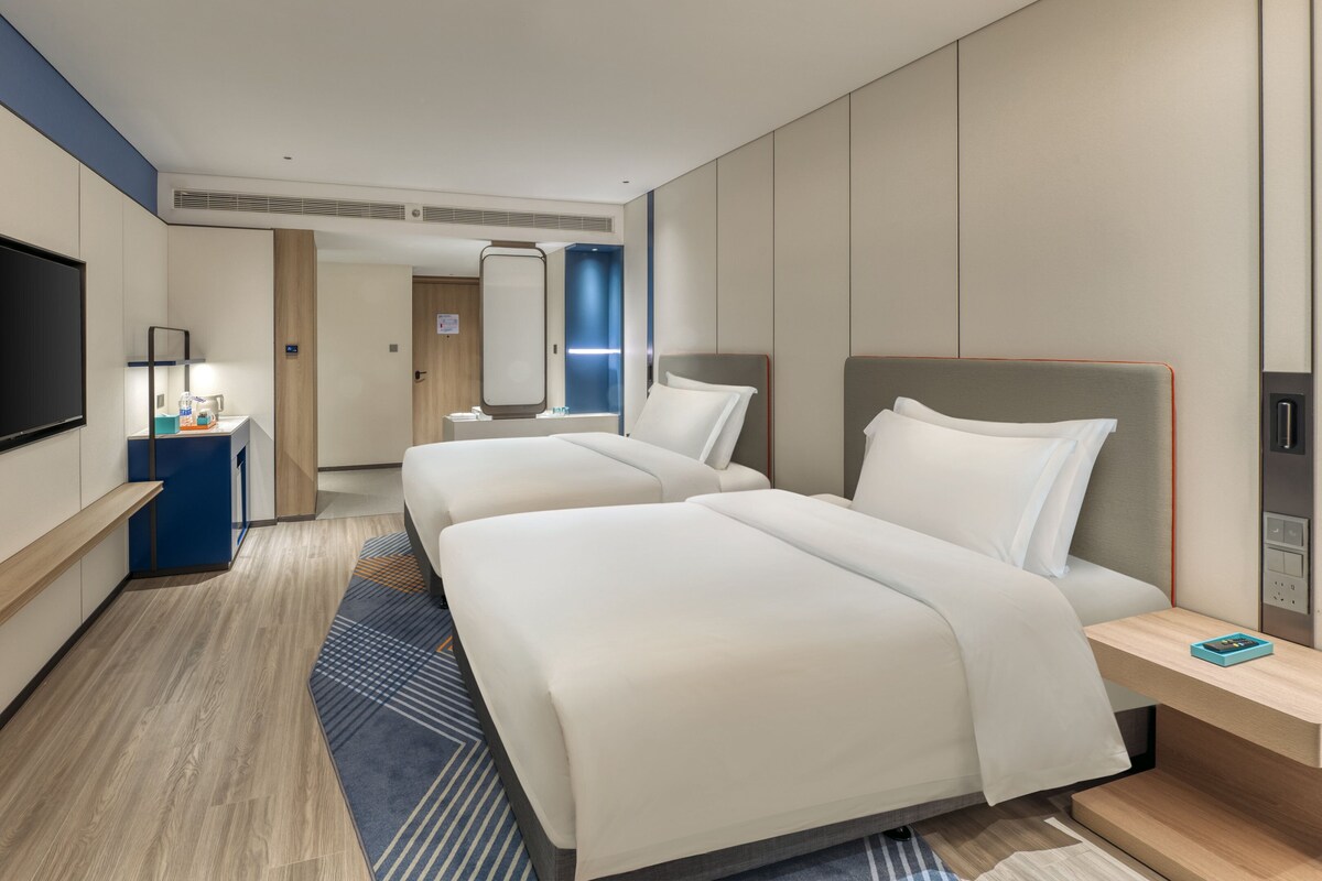 A hotel room with two beds, a TV, a desk, and a bathroom visible in the background.
