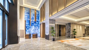 A spacious lobby with a high ceiling, marble flooring, and a large abstract blue and gold mural. - Rugao City Center by IHG (Nantong)