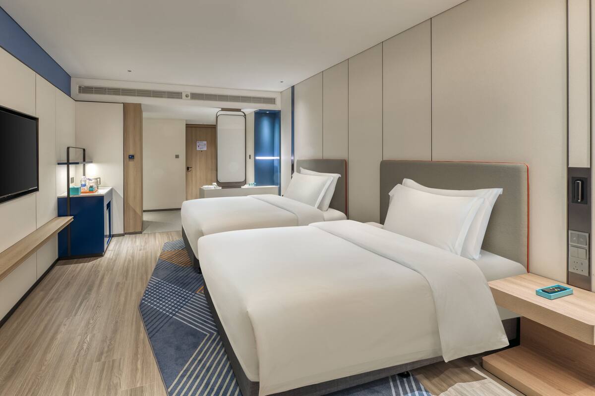 A hotel room with two beds, a TV, a desk, and a bathroom visible in the background.