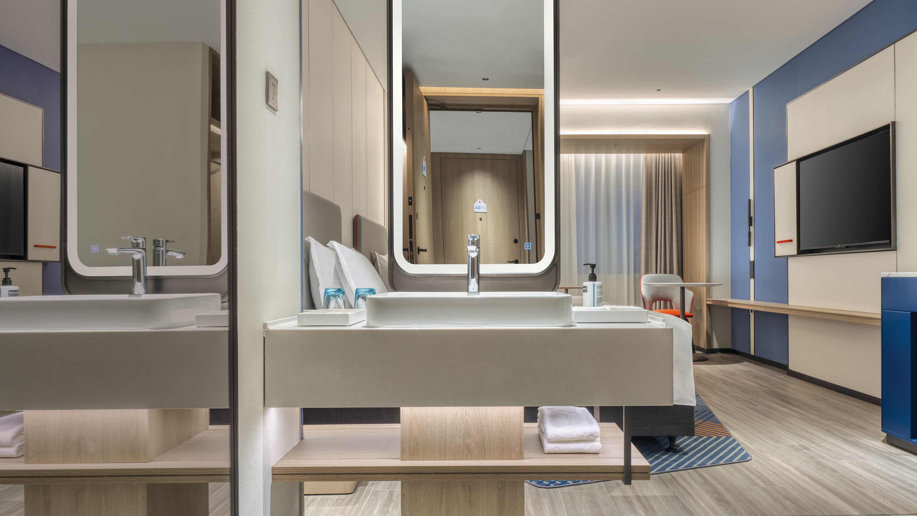 A modern hotel bathroom with a large mirror, a sink, and a toilet.