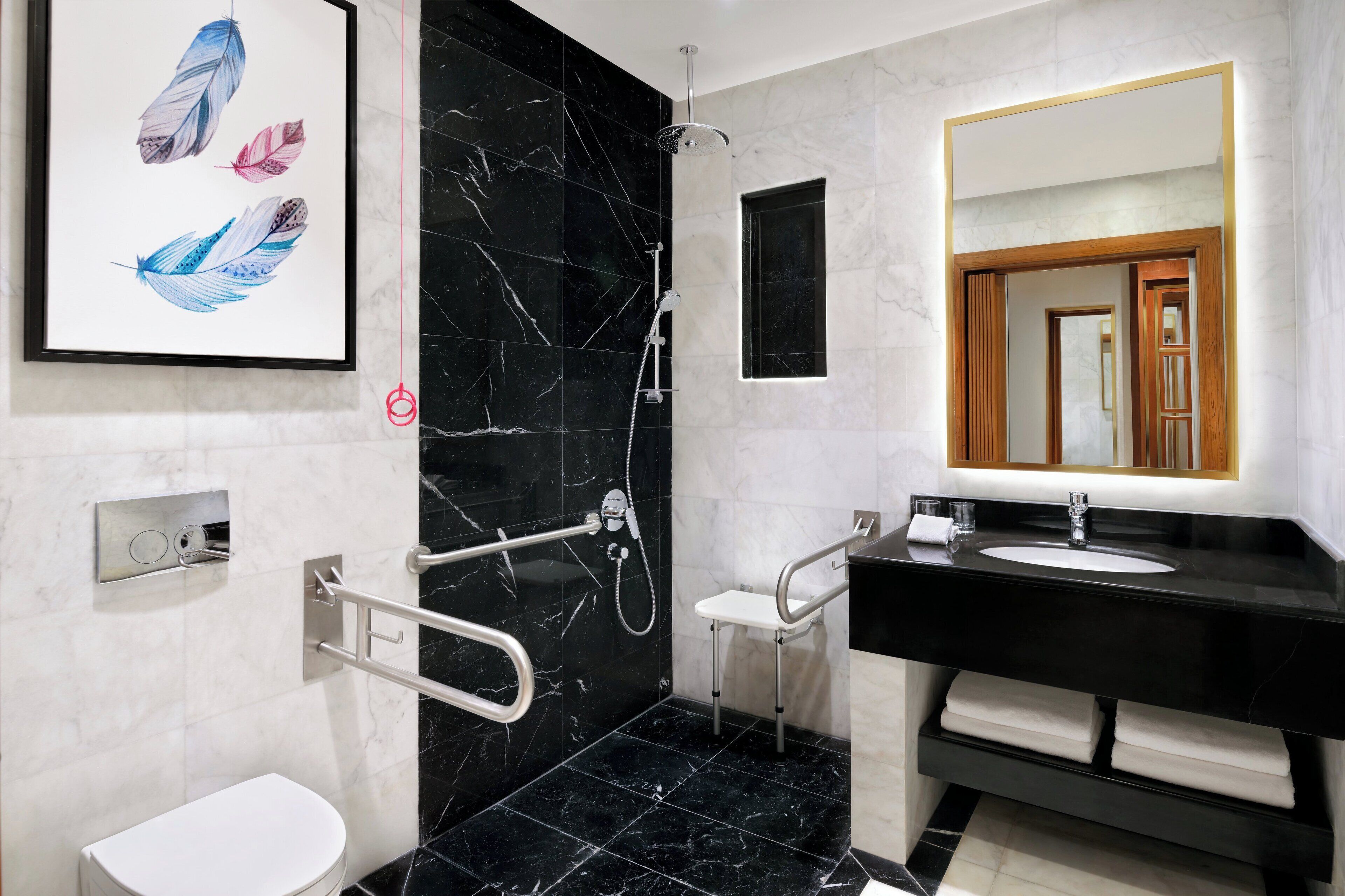 Un baño moderno con pared de mármol negro, inodoro blanco, lavamanos con espejo y ducha con cabezal de ducha manual.