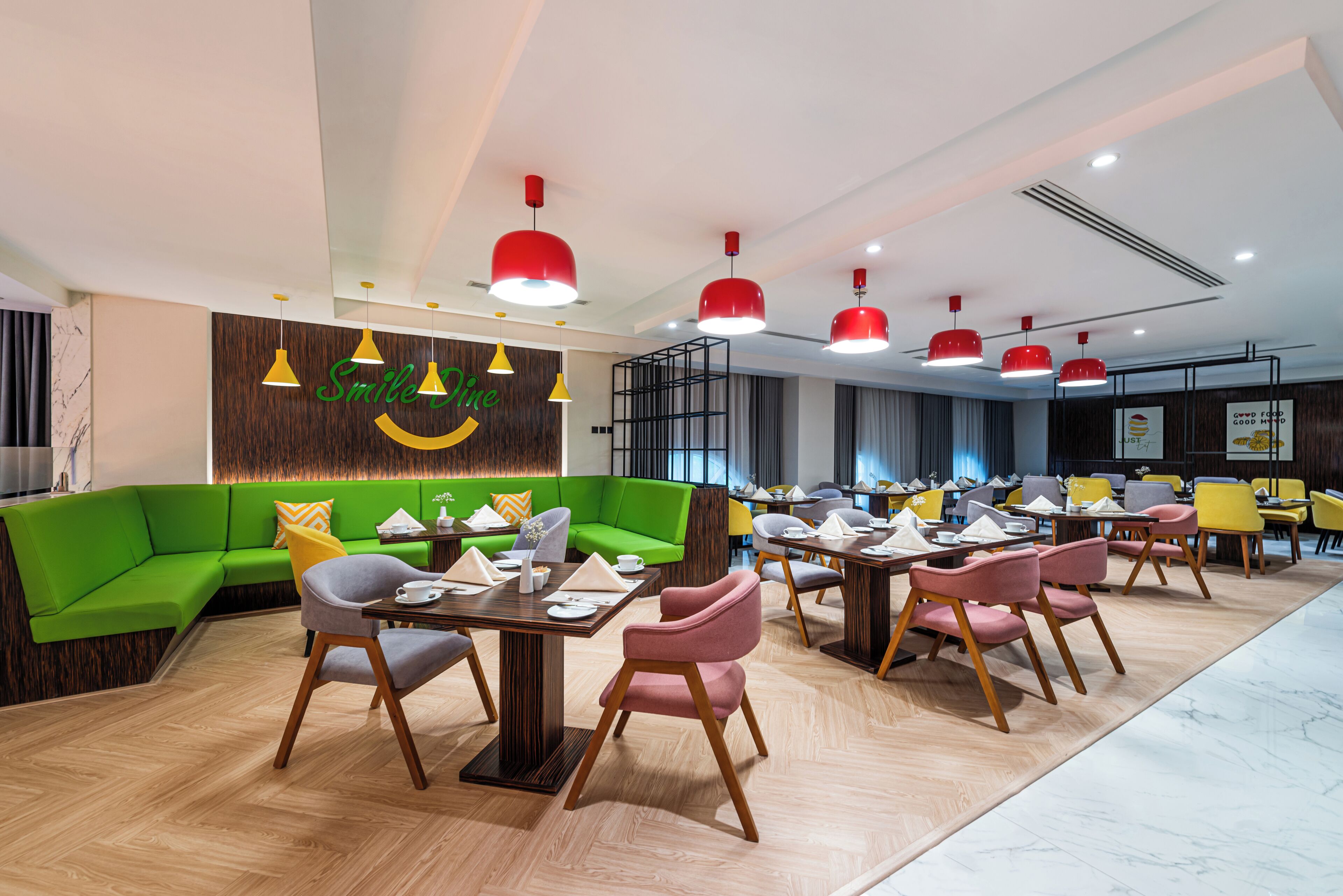 A modern dining area with green sofas, wooden tables, and red pendant lights.
