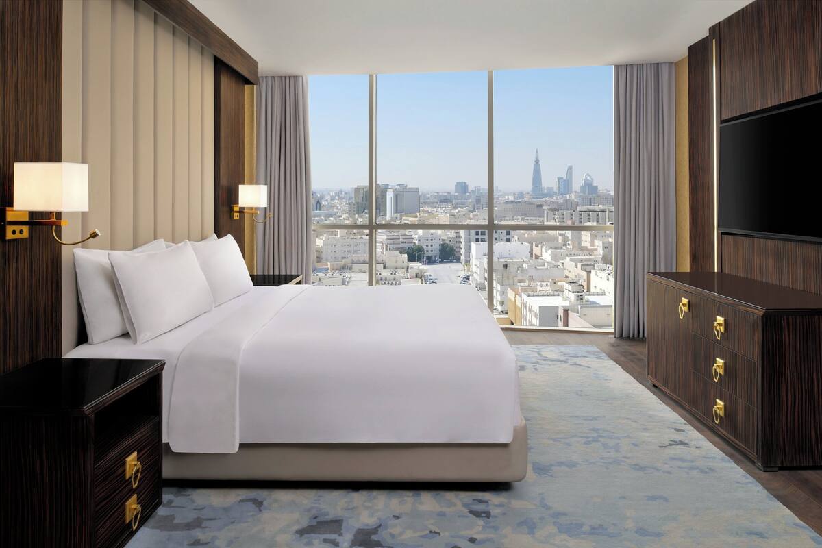 A modern hotel room with a large bed, a TV, and a city view.