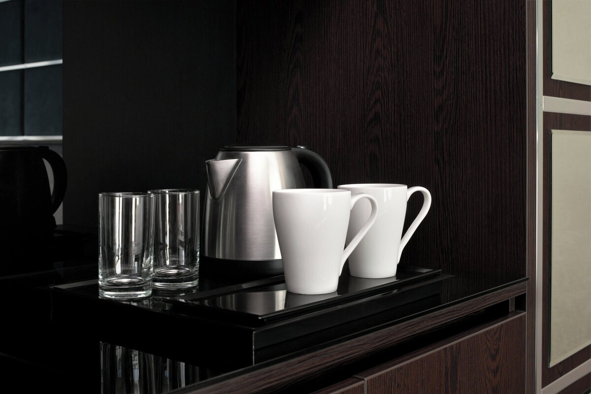 A modern kitchen with a black countertop, stainless steel kettle, and white mugs.