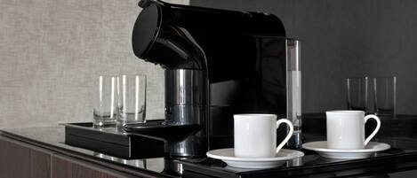 A modern coffee station with a black coffee maker, two white cups, and two clear glasses on a reflective black countertop.