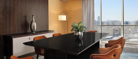 Une salle de conférence moderne, dotée d’une table noire, de chaises orange, d’une plante en pot et offrant une vue sur la ville grâce à de grandes fenêtres.