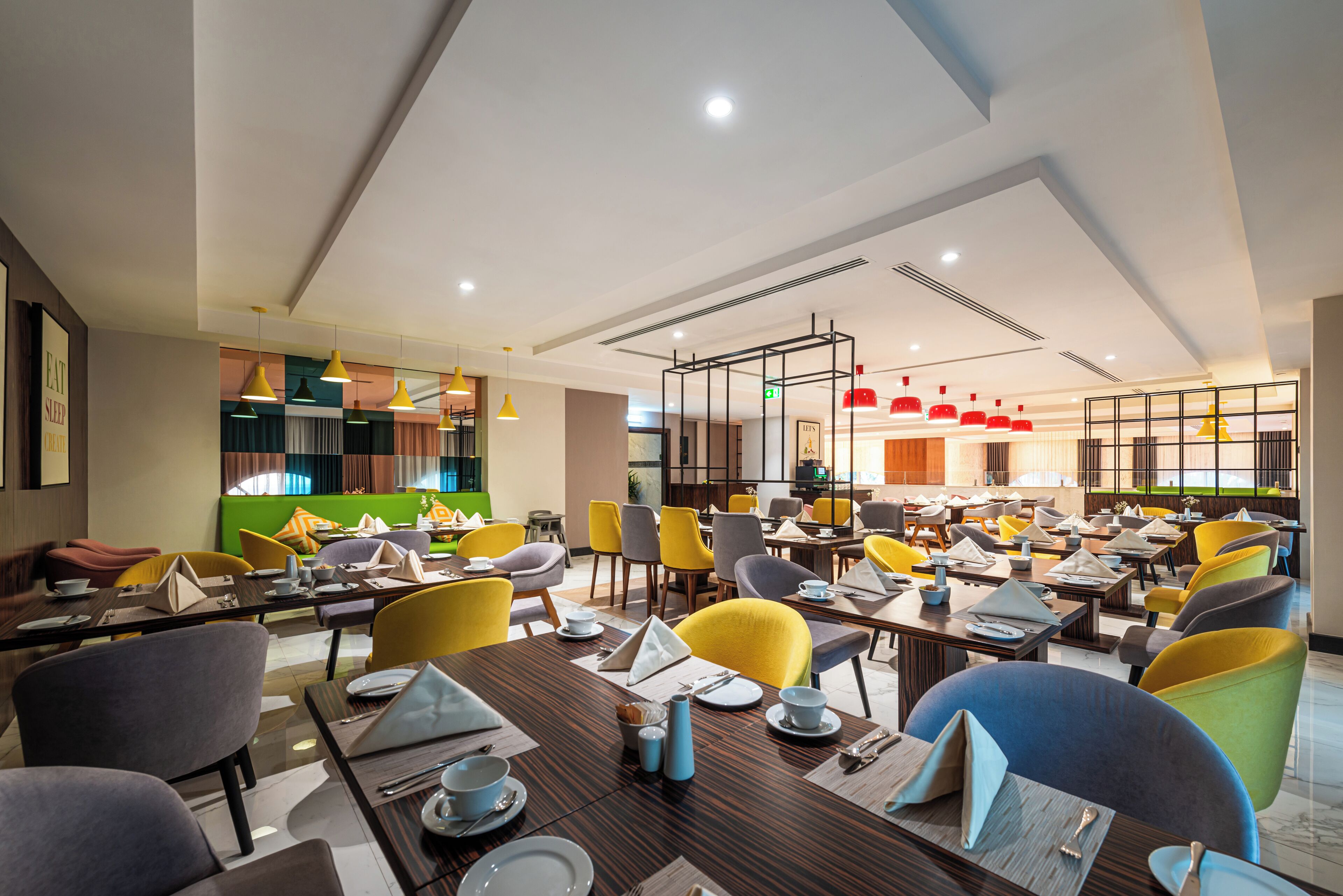 A modern restaurant with multiple dining tables and chairs, a kitchen area, and a variety of pendant lights.