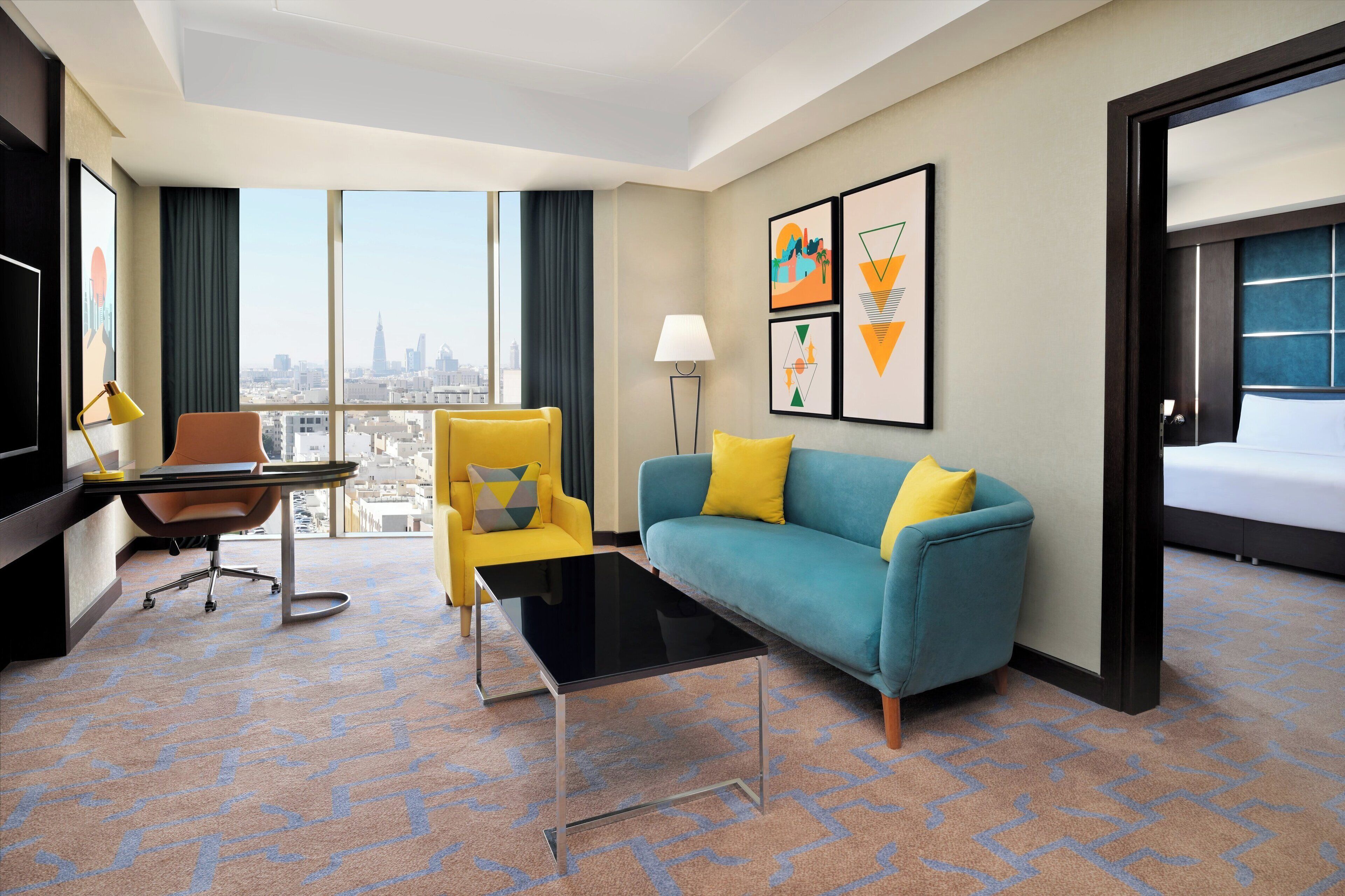 A hotel room with a large window, a sofa, a chair, a desk, and a bed.