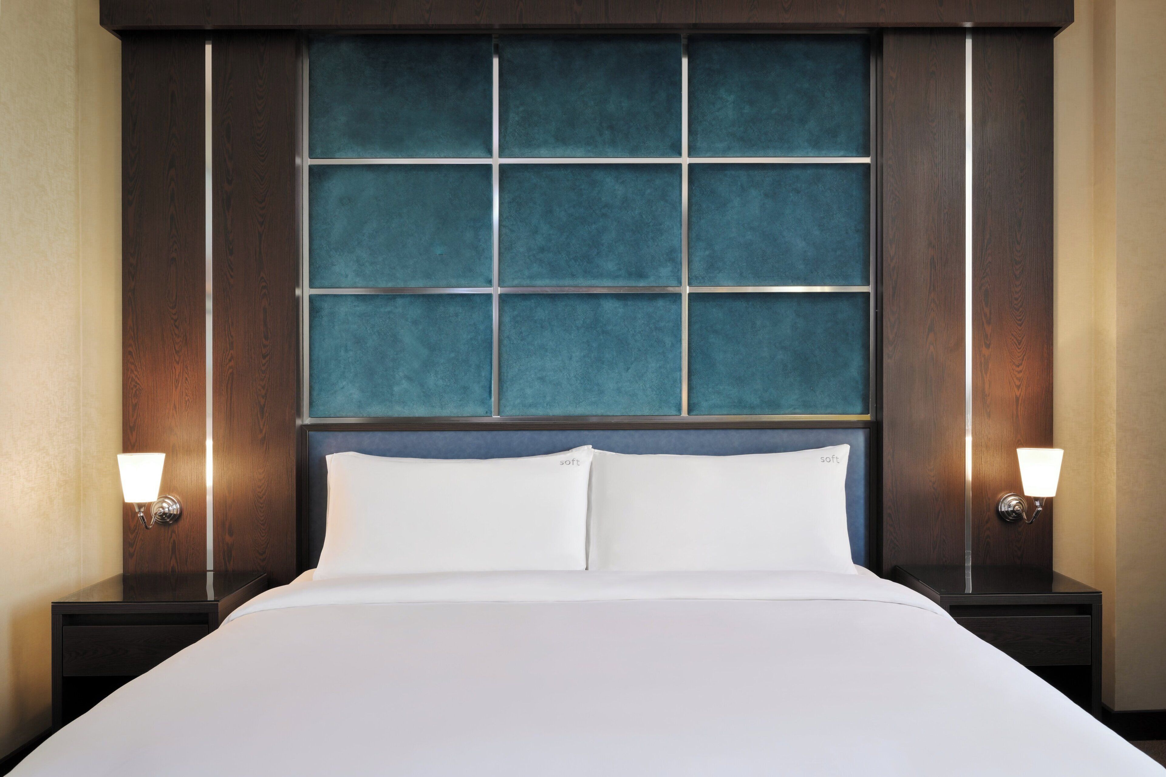 A hotel room with a large bed, two bedside tables, and a headboard with a blue panel.