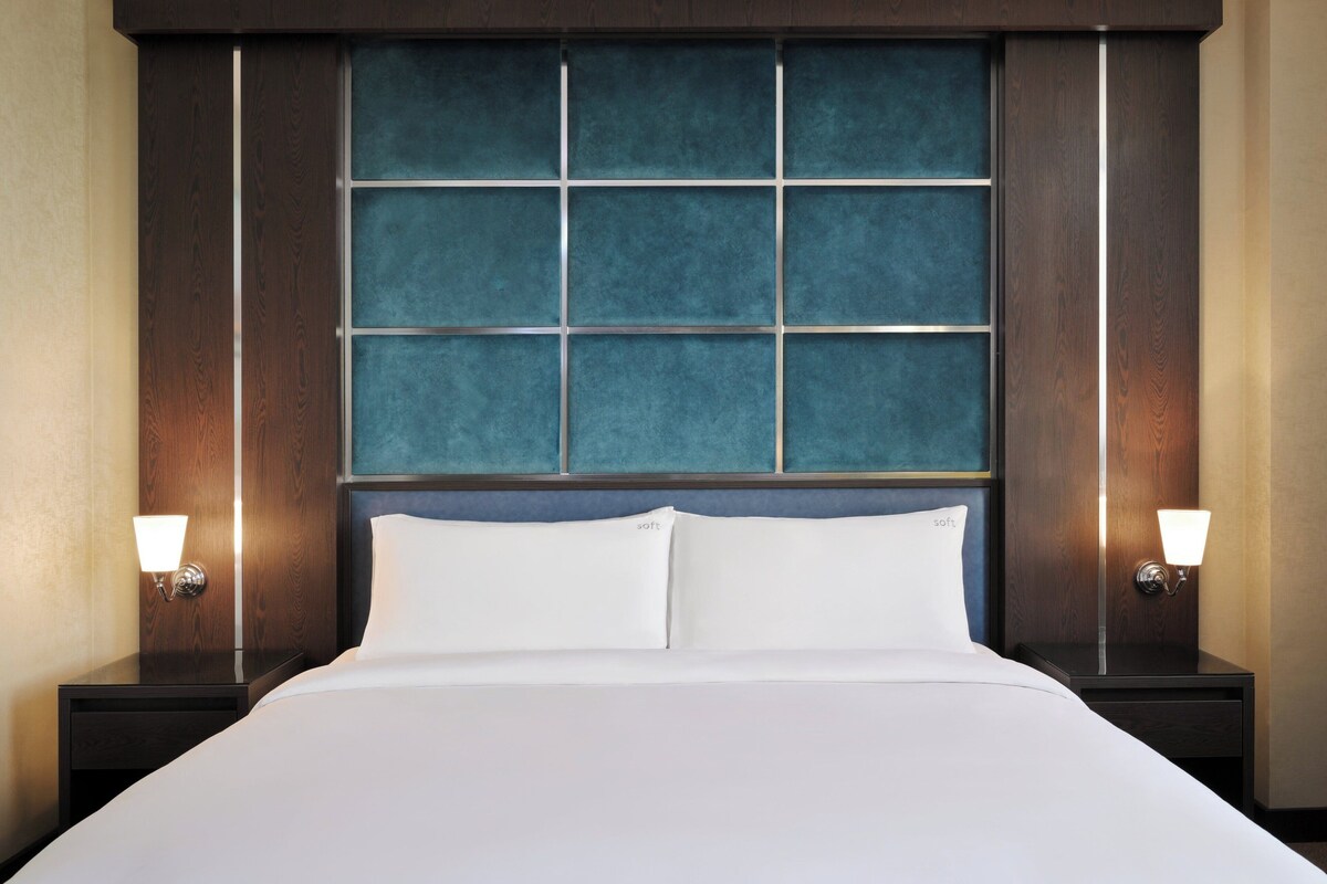 A hotel room with a large bed, two bedside tables, and a headboard with a blue panel.
