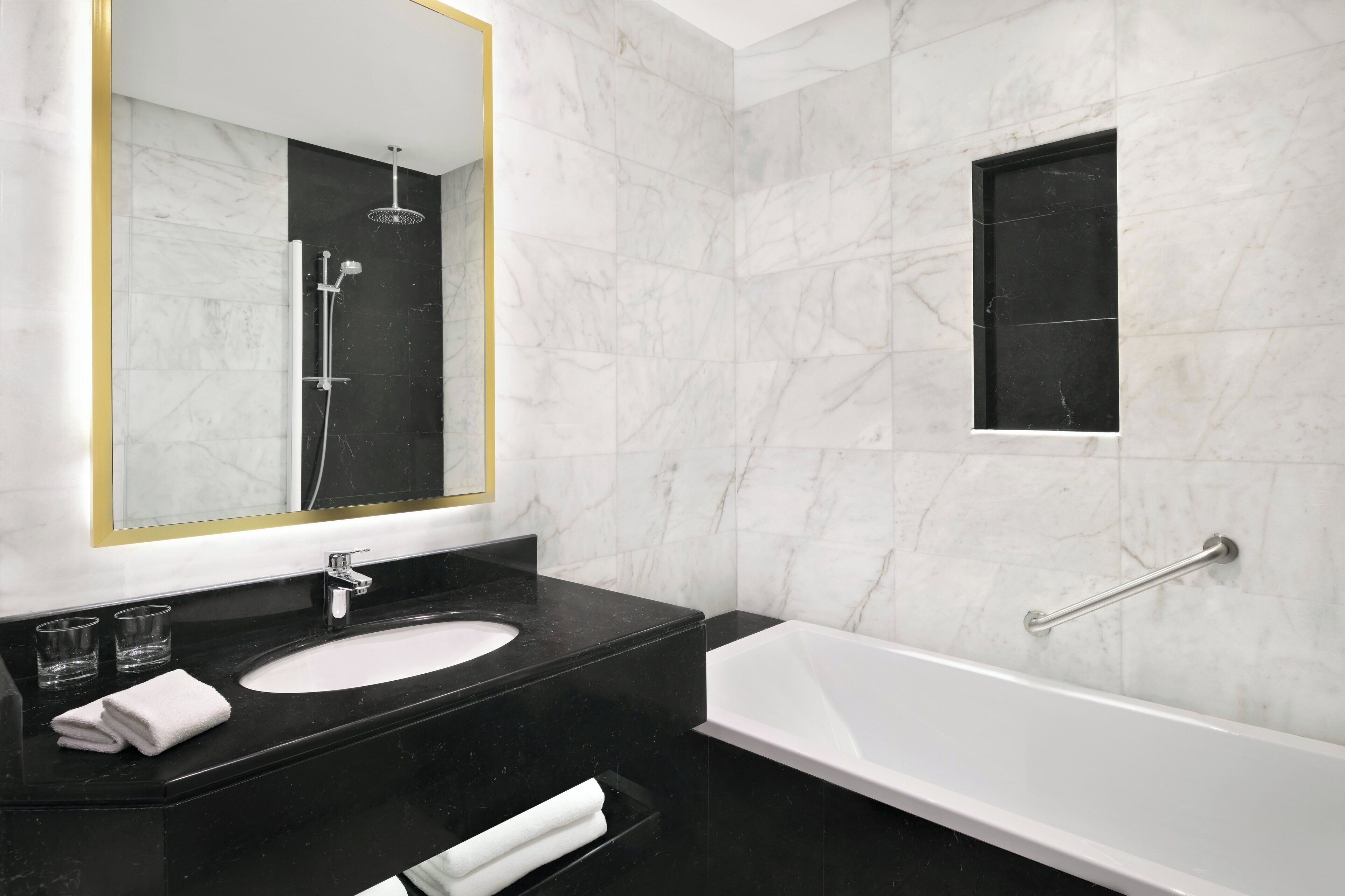 A modern bathroom with a black marble vanity, a white sink, and a white bathtub.