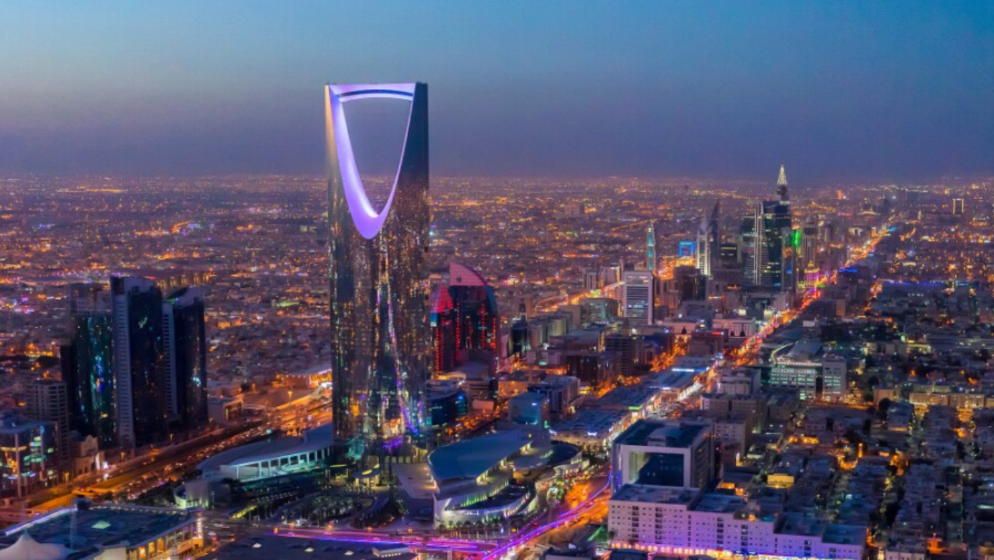 A cityscape with a prominent modern skyscraper featuring a unique curved design and illuminated purple lighting.