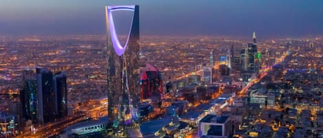 A cityscape with a prominent modern skyscraper featuring a unique curved design and illuminated purple lighting.