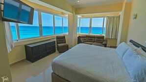 A bedroom with a large bed, two armchairs, a TV, and a view of the ocean. - Beachfront – 11BR/9Bth – Penthouse Combo #3120 (Cancun)