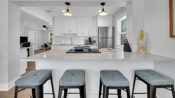 A modern kitchen with white cabinetry, a stainless steel refrigerator, and a central island with bar stools. - Winter Getaway Stuart - Bring your truck, boat or RV - Large Fenced Yard (Stuart)