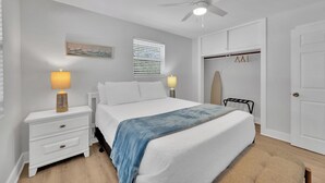 A bedroom with a bed, nightstands, a ceiling fan, a window with blinds, a coat rack, and a door. - Winter Getaway Stuart - Bring your truck, boat or RV - Large Fenced Yard (Stuart)